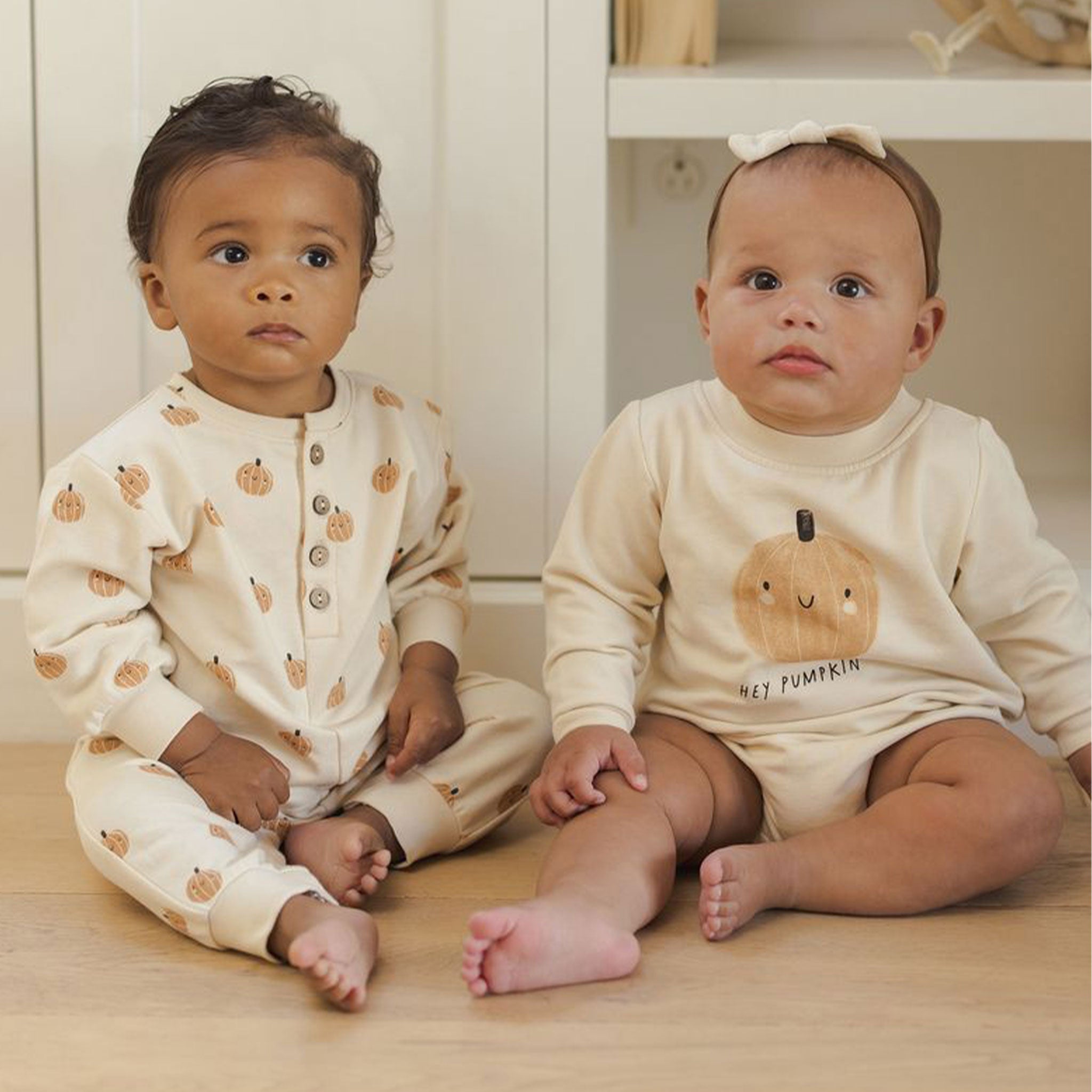 Two babies wearing pumpkin onesies.