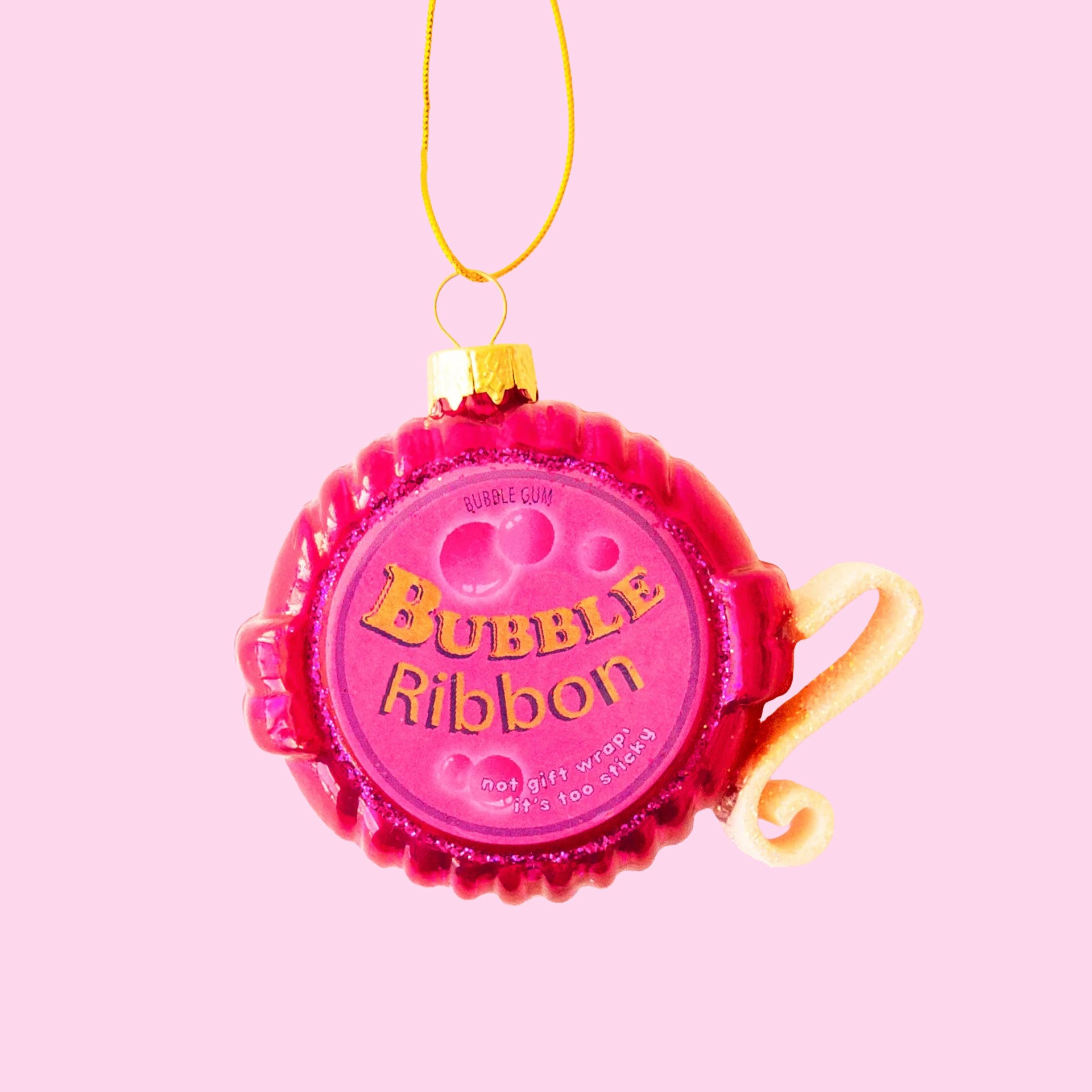 On a pink background is a bright pink Bubble Gum Tape Dispenser ornament with a gold loop for hanging.