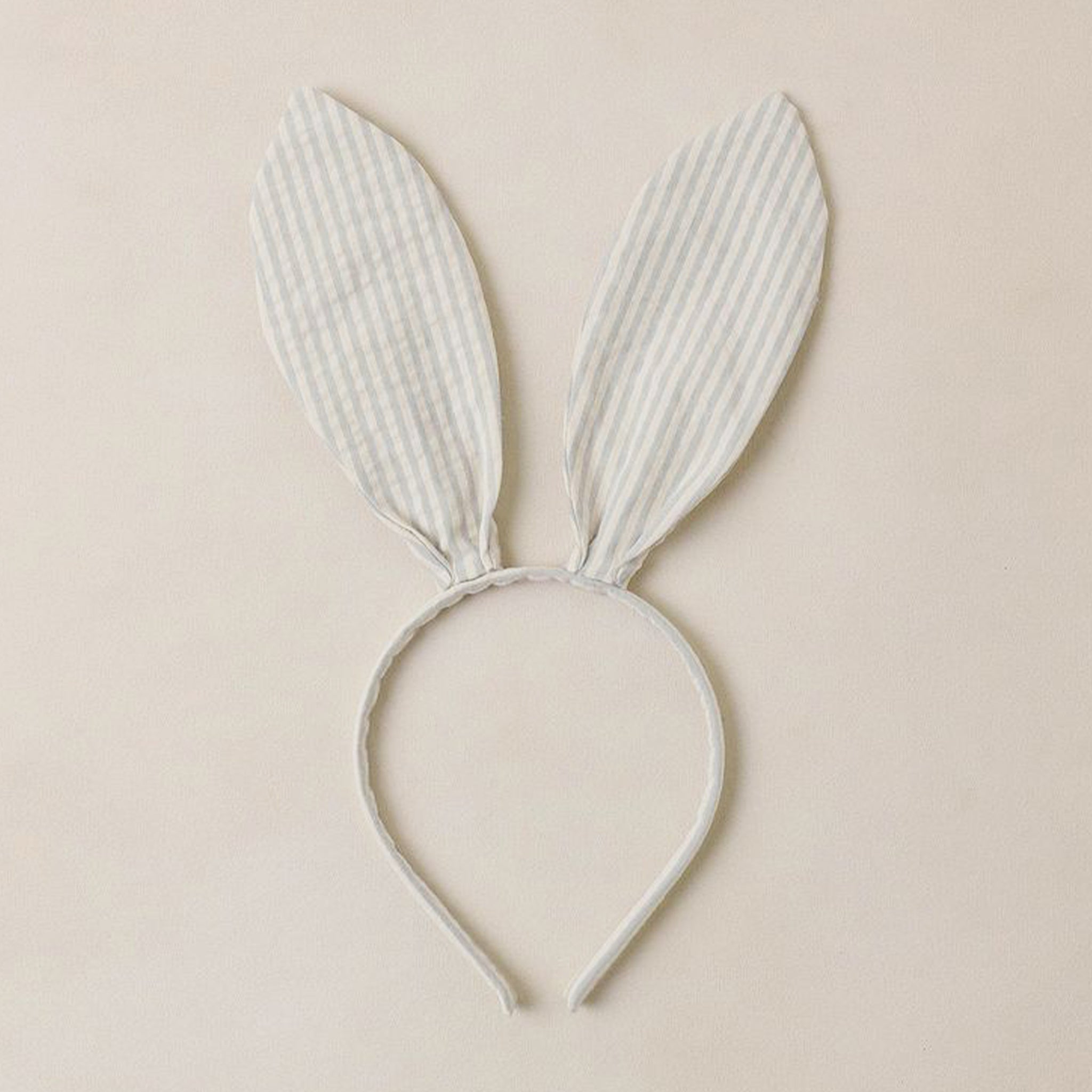 A bunny ear shaped headband with a light blue and cream stripe pattern. 