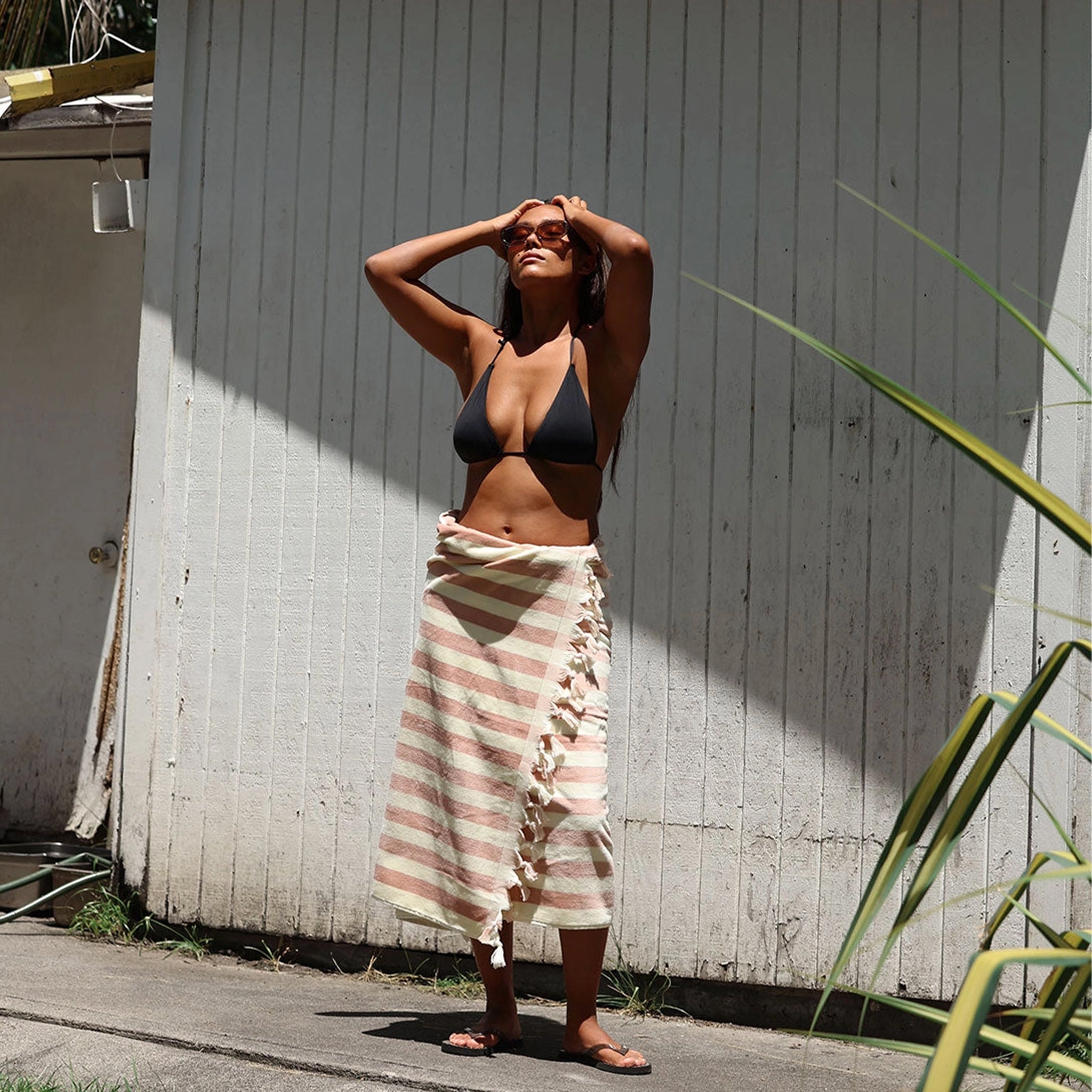Woman in a black bikini and striped towel standing against a light-colored wall.