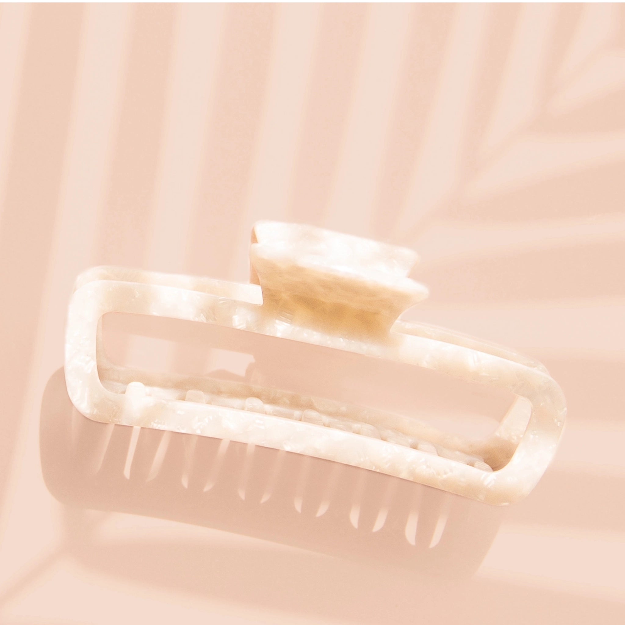 On a light pink background is an ivory rectangle claw clip with a pearl finish detail and slightly rounded edges. 