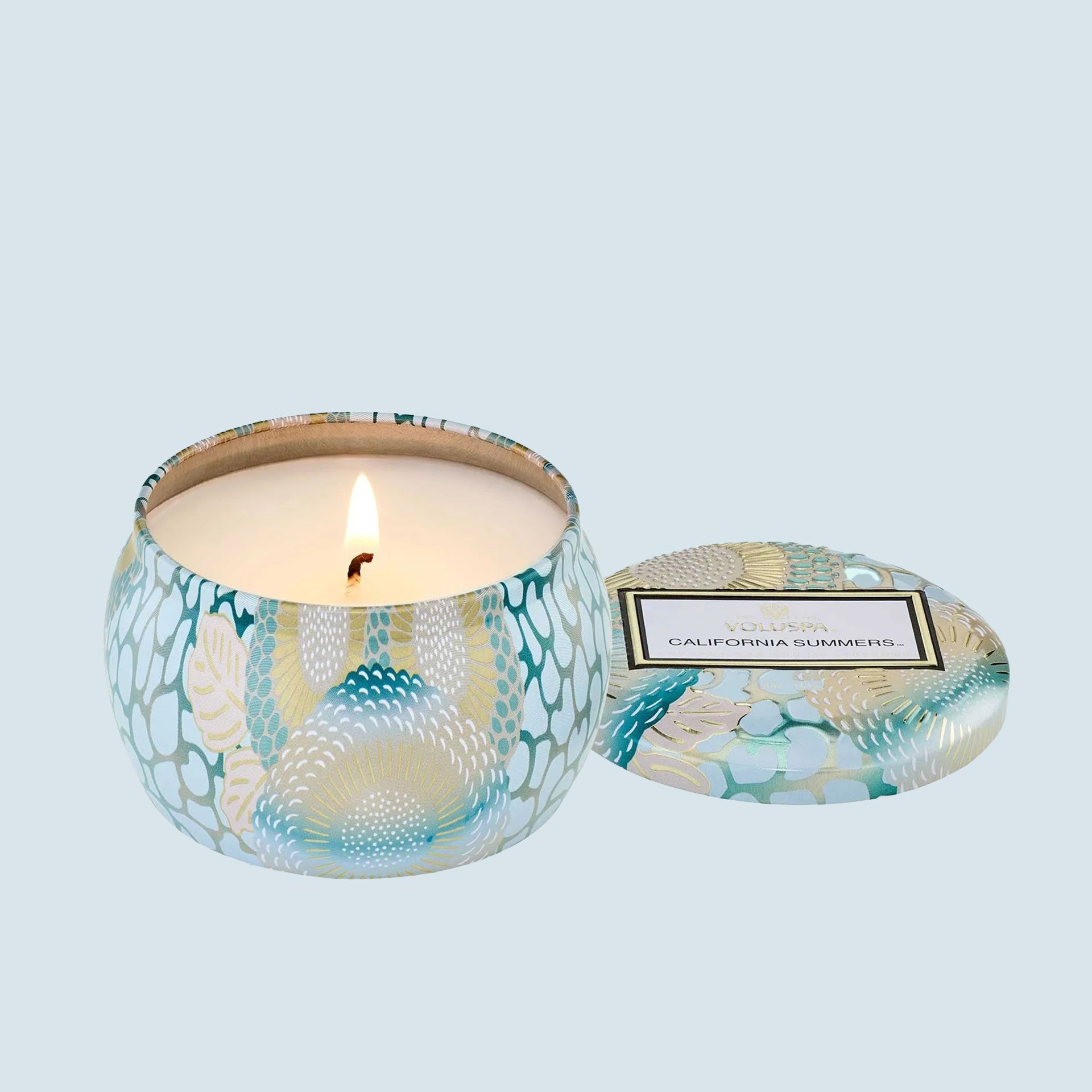 On a blue background is a light blue decorative mini tin candle with a lid and a rectangle label that reads, "Voluspa California Summers". 