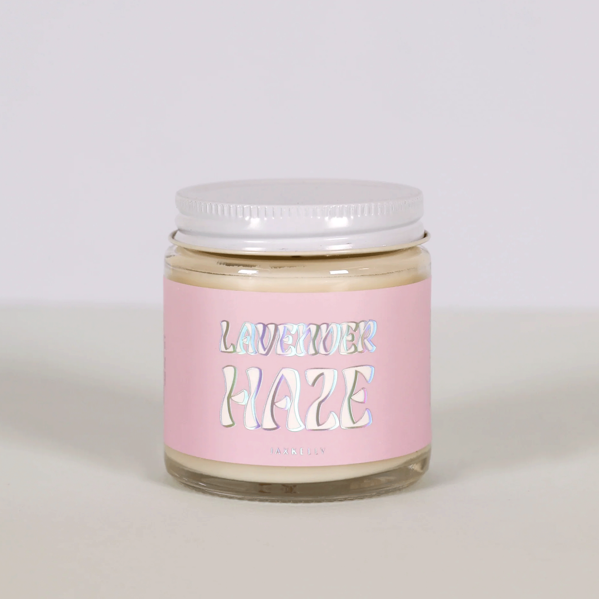 On a white background is a 4oz glass jar candle with a light pink label that reads, &quot;Lavender Haze&quot; in a holographic wavy font.