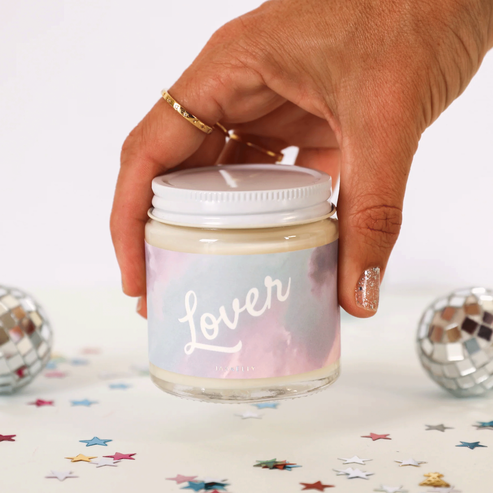 A pink and purple cloud label that reads, &quot;Lover&quot; on a glass jar candle with a white lid.