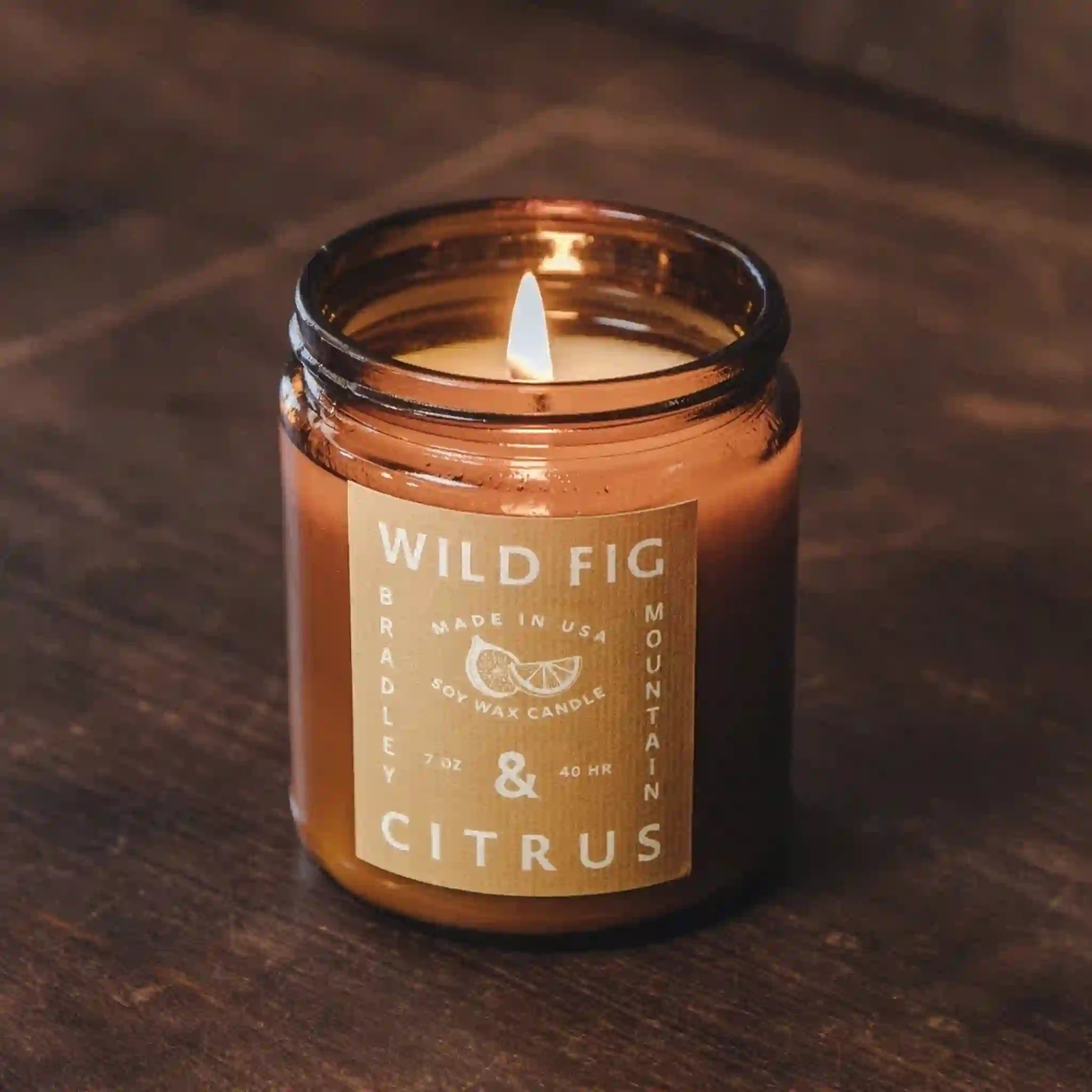 On a brown background is an amber colored jar candle with a yellow label and white text that reads, &quot;Wild Fig &amp; Citrus&quot;.
