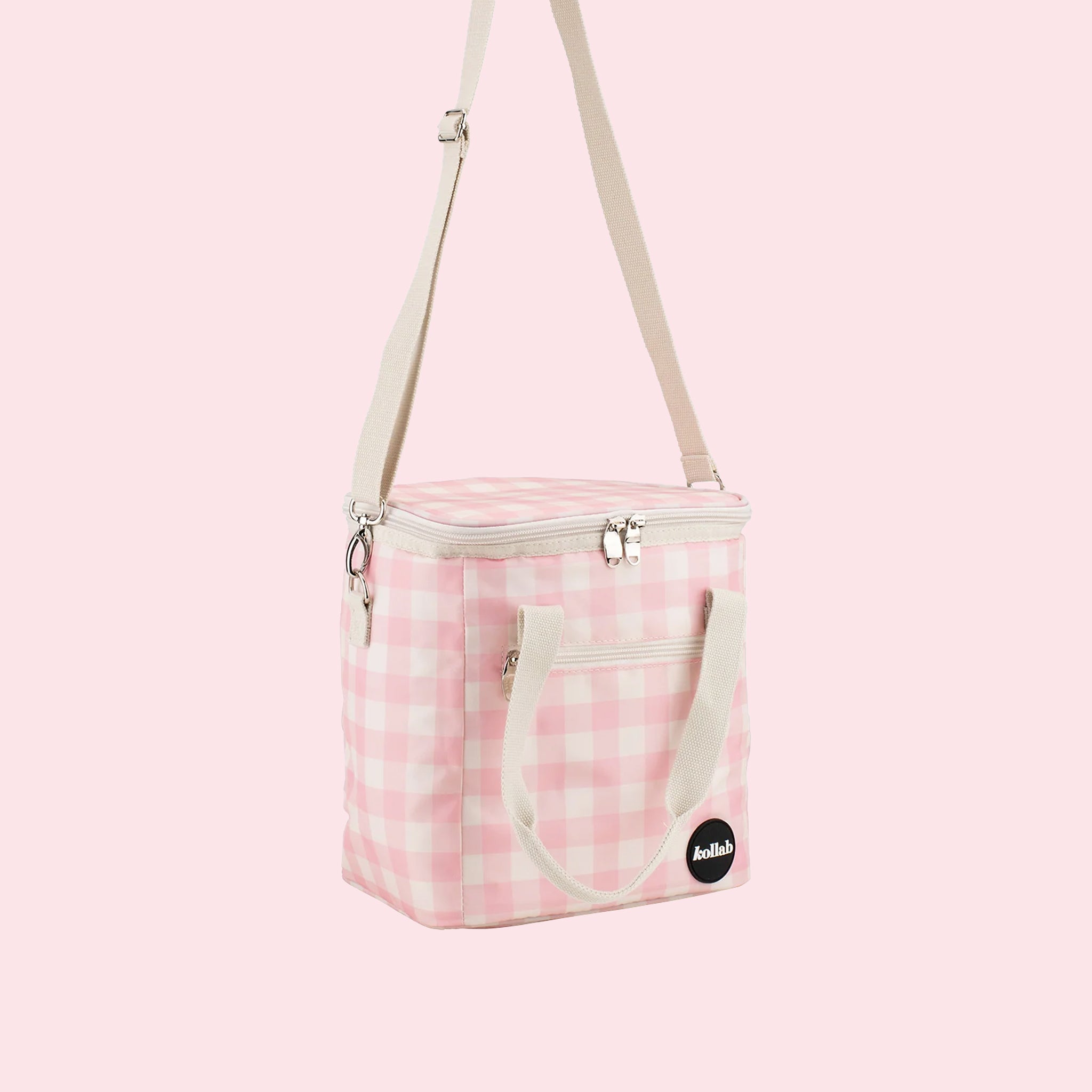On a light pink background is a pink and white cooler bag with a long adjustable strap. 