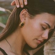 Close-up of a woman wearing gold earrings with a blurred natural background