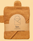 On a yellow background is a caramel orange colored bath towel for kids with a hood and bear ears on the hood.