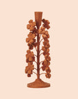 A terracotta colored cast iron taper candle holder with flower shapes on the sides. 