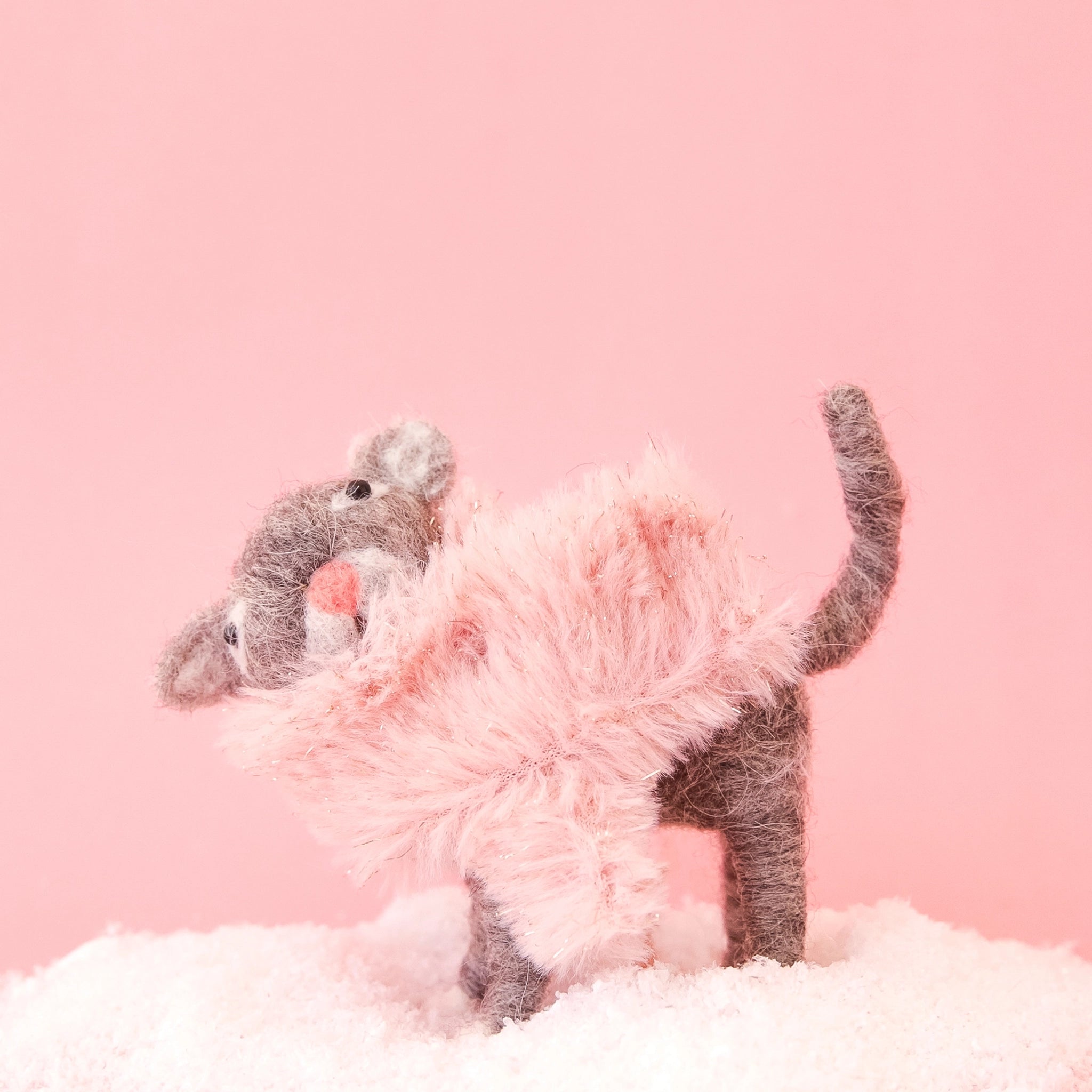 On a pink background is a brown felt cat ornament with a pink fluffy faux fur scarf.