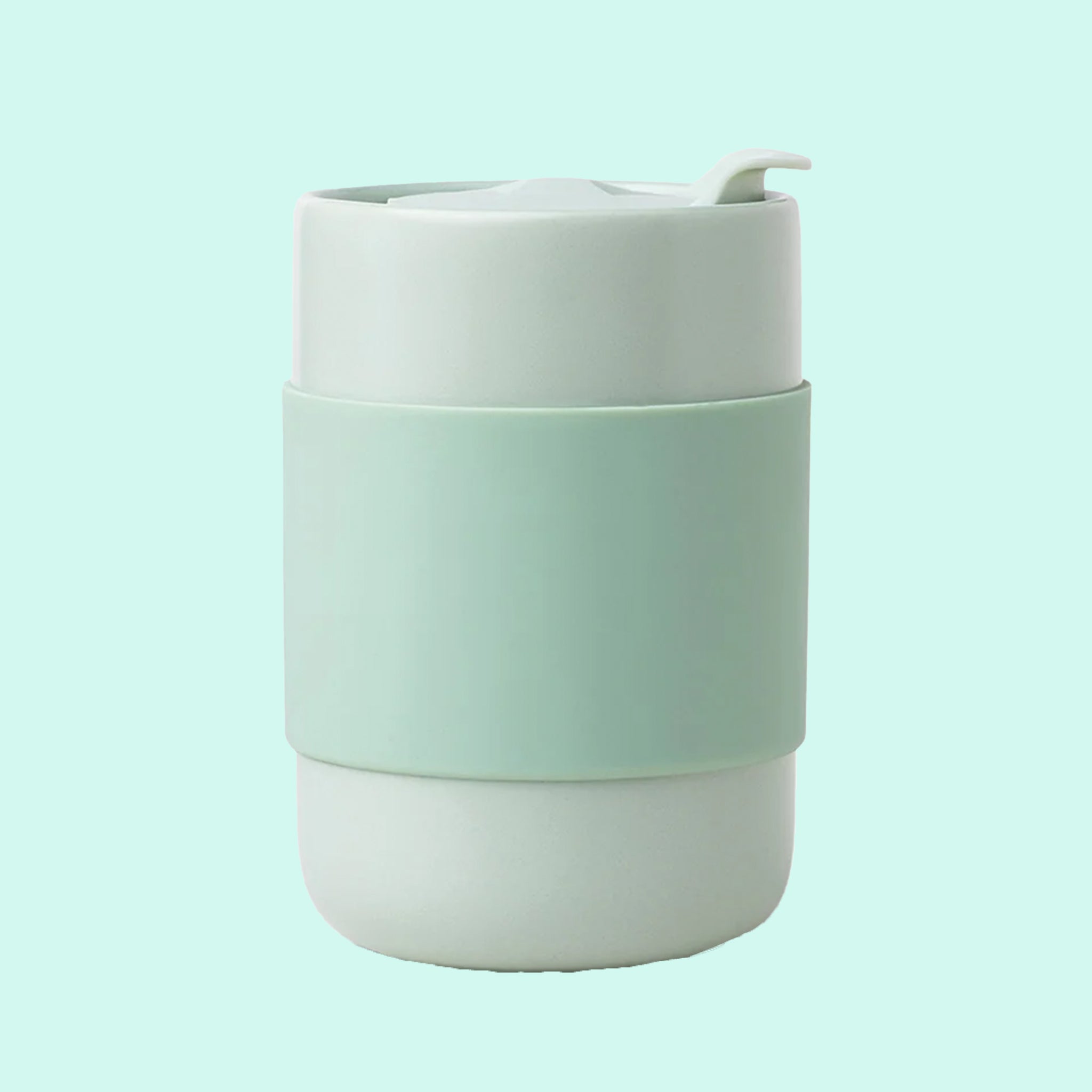 On a mint green background is a mint green ceramic tumbler with a silicone sleeve. 