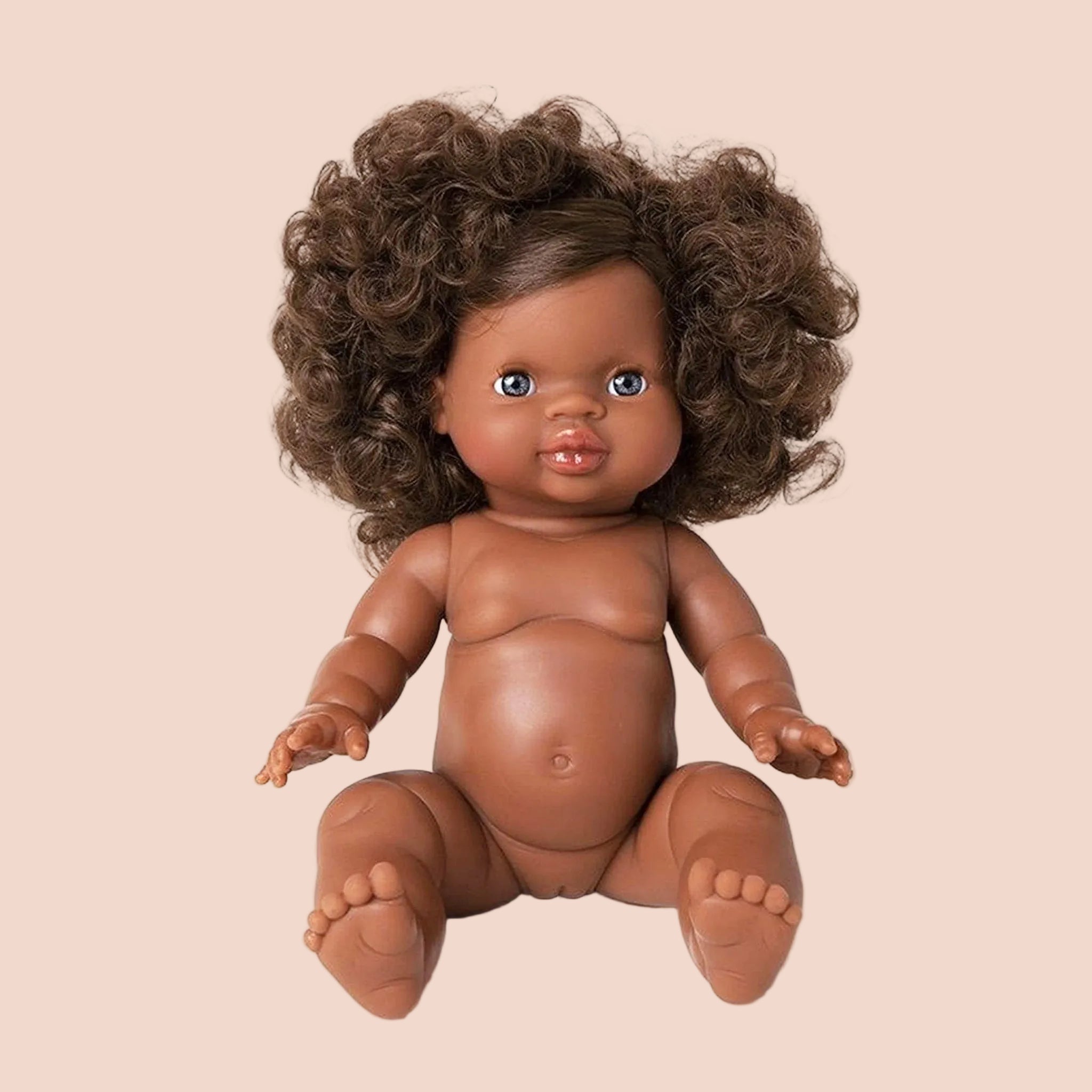 In front of a white background is a baby doll with dark brown curly hair.