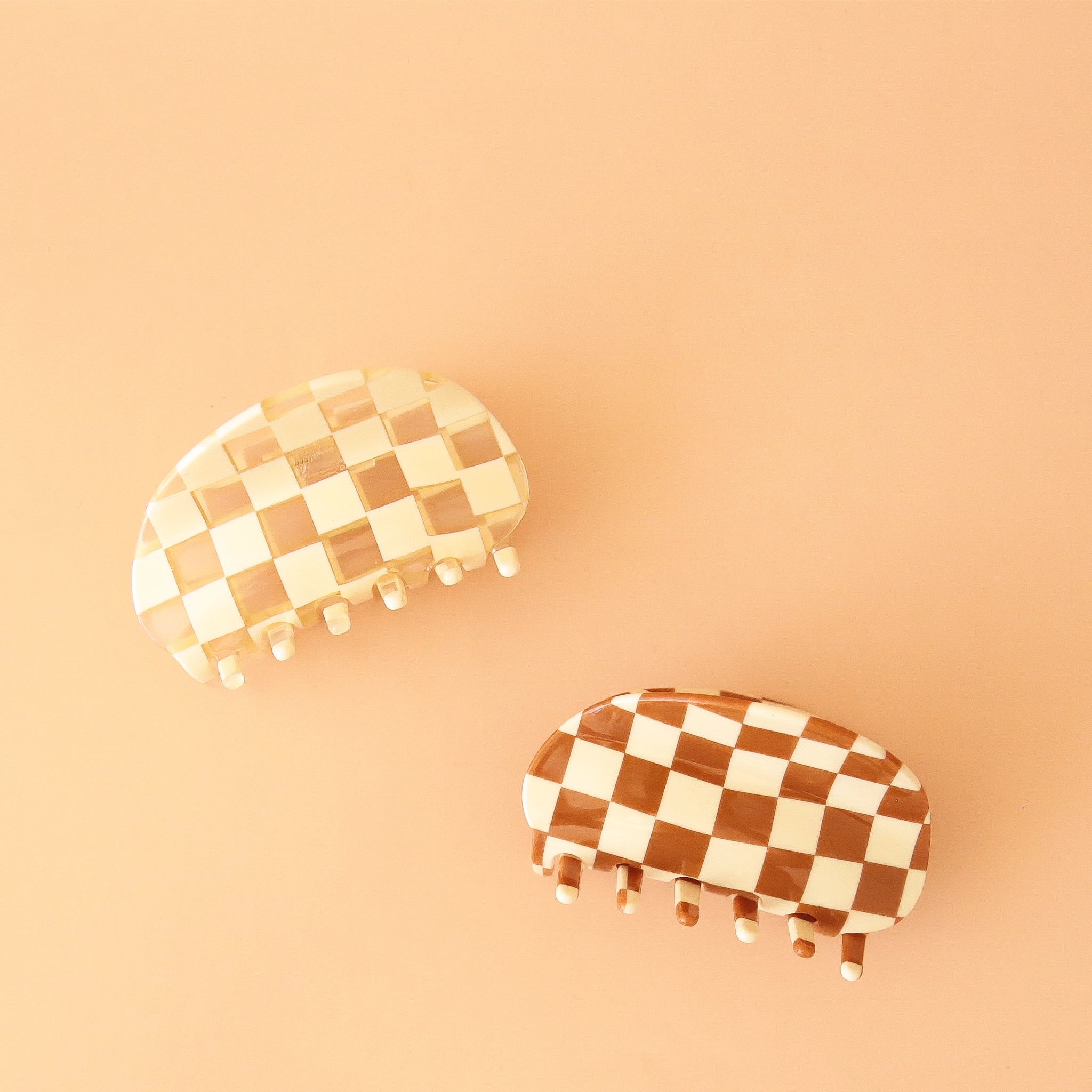 The rounded white and clear checker claw clip photographed with a brown and cream checkered claw clip with the same shape. 