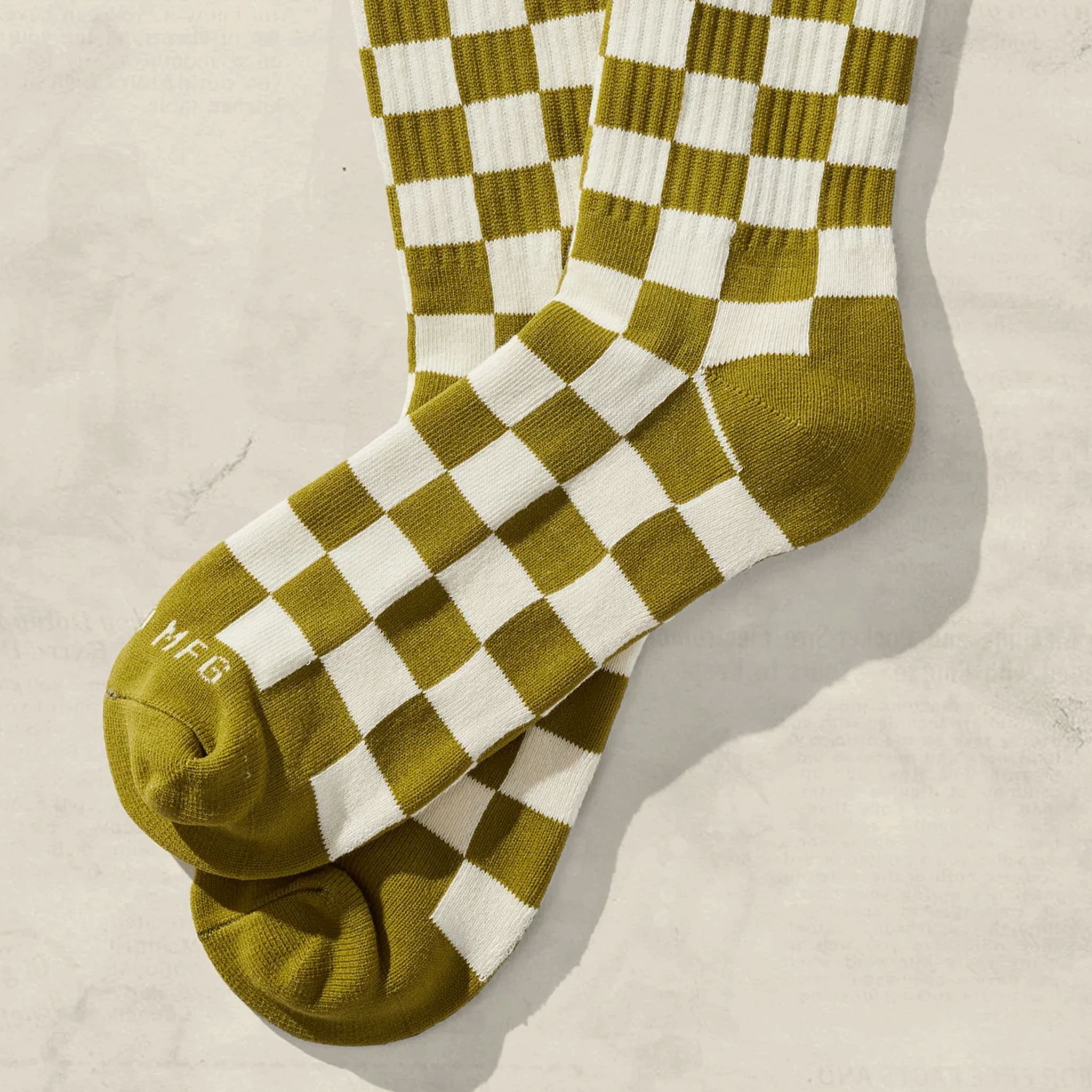 On a cream background is a pair of green and ivory checkered socks.