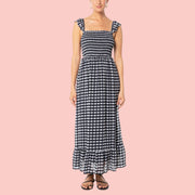 A model wearing a black and white gingham printed dress with a smocked body and flutter arm straps. 