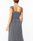 A model wearing a black and white gingham printed dress with a smocked body and flutter arm straps