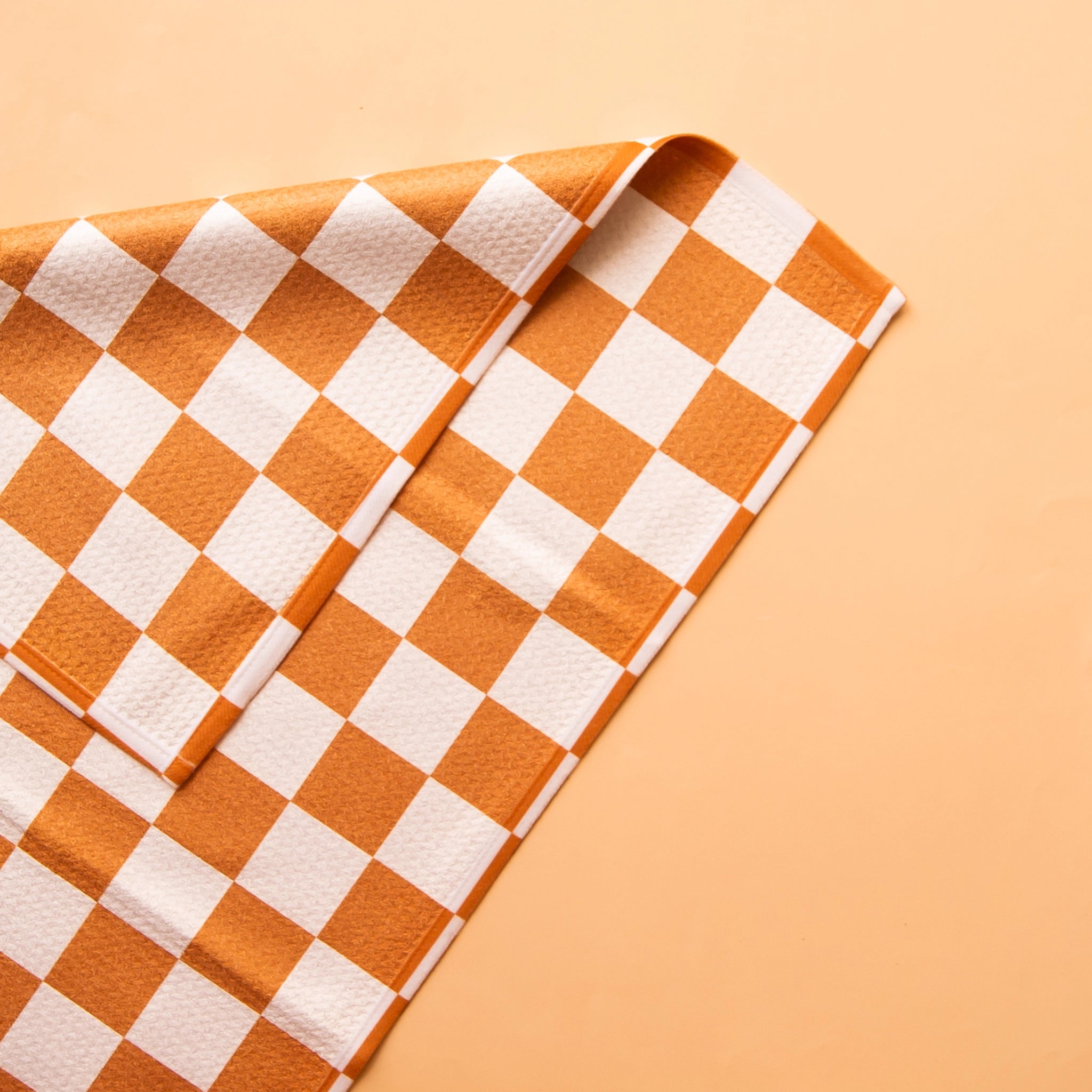 On an orange backdrop is an orange and ivory checkered kitchen towel.