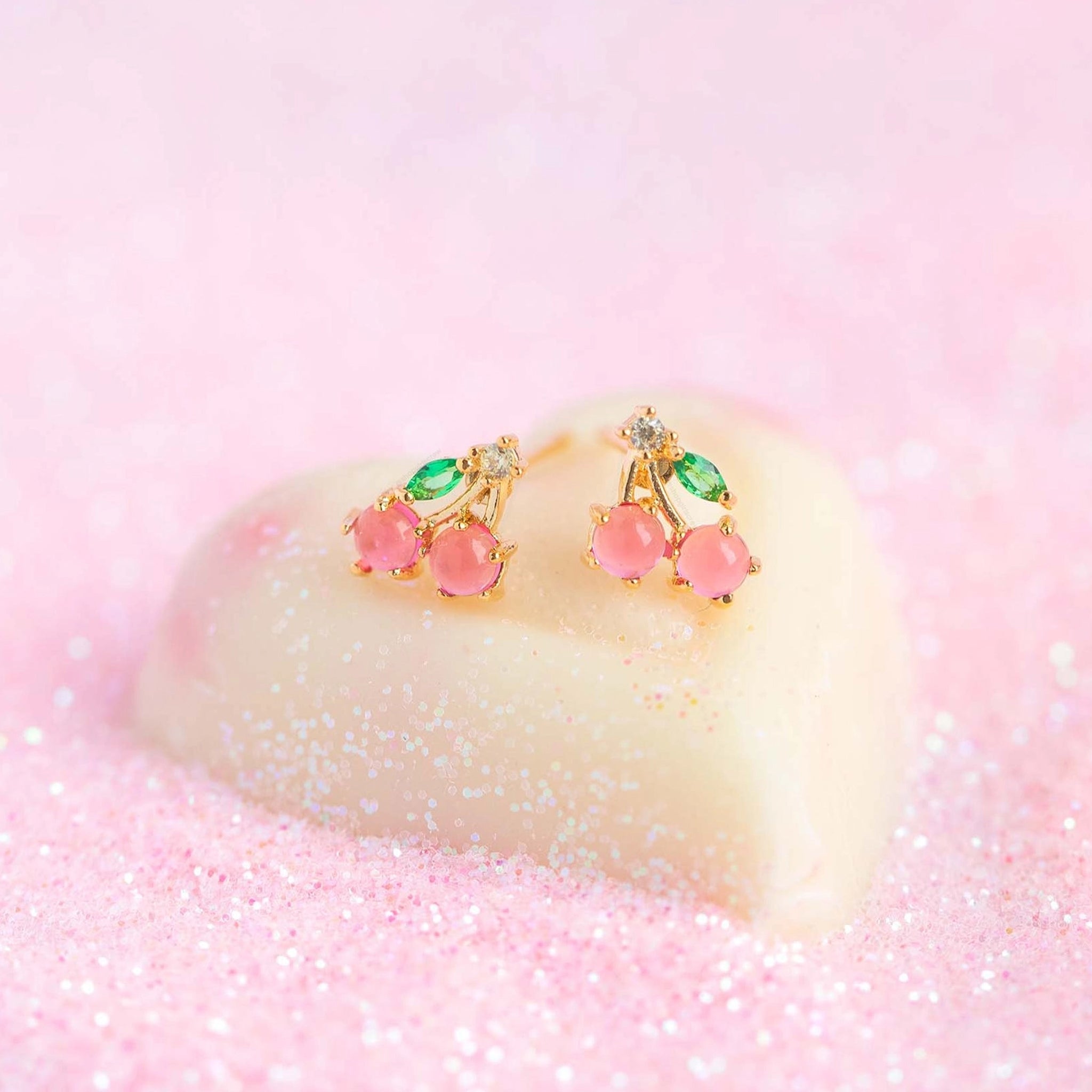 A pair of pink and green cherry shaped stud earrings. 