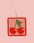 A square air freshener with a graphic of two cherries. 