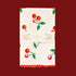 a folded tea towel sits on a pink background.  The towel is a white color with red cherries with green leaves scattered across the fabric.  There is a band of paper across the middle of the folded towel that reads "tea towel".