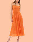 On a peach background is vibrant orange tiered midi dress with a smocked bodice and spaghetti straps. 