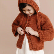 A model wearing this children's knit cardigan in a spiced brown/orange shade. 