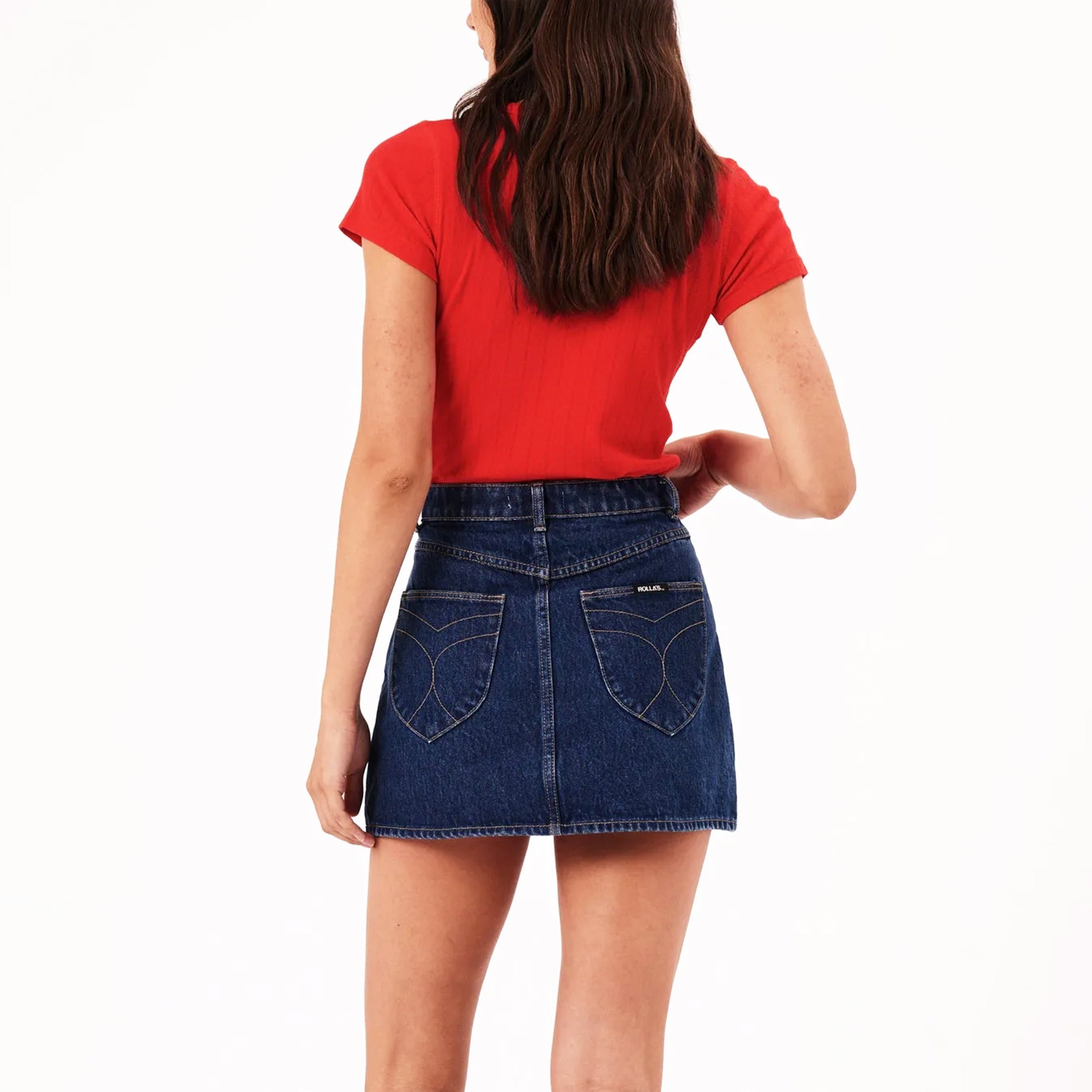 A model wearing a dark blue denim mini skirt with back pockets. 