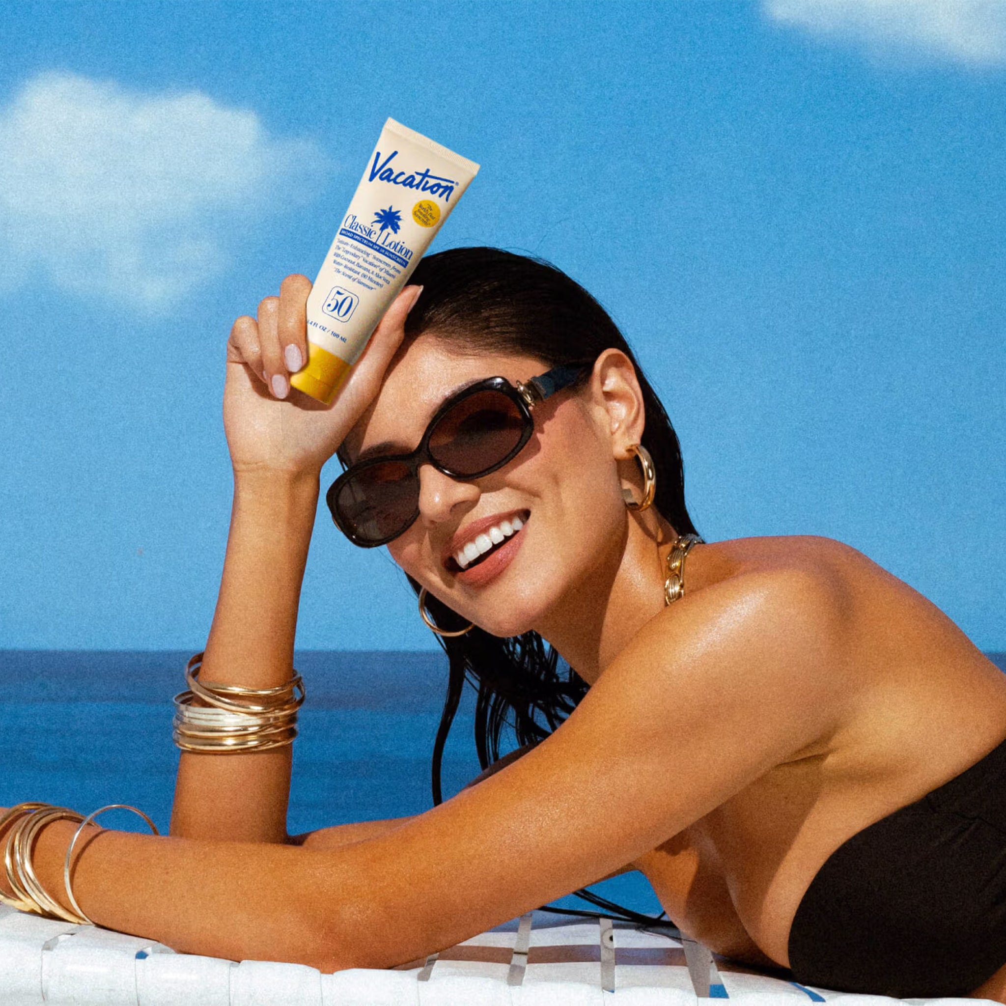 Woman holding a sunscreen tube with a blue sky and ocean background