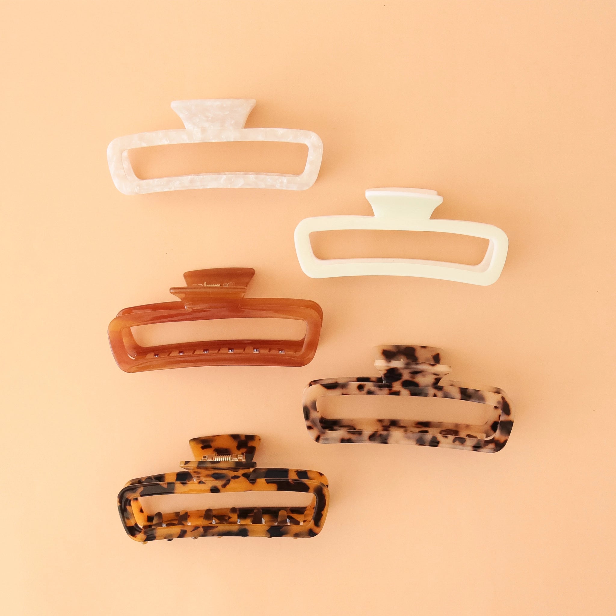 On a peachy background is a variety of rectangle claw clips in tortoise shades, an amber color and two different whites.