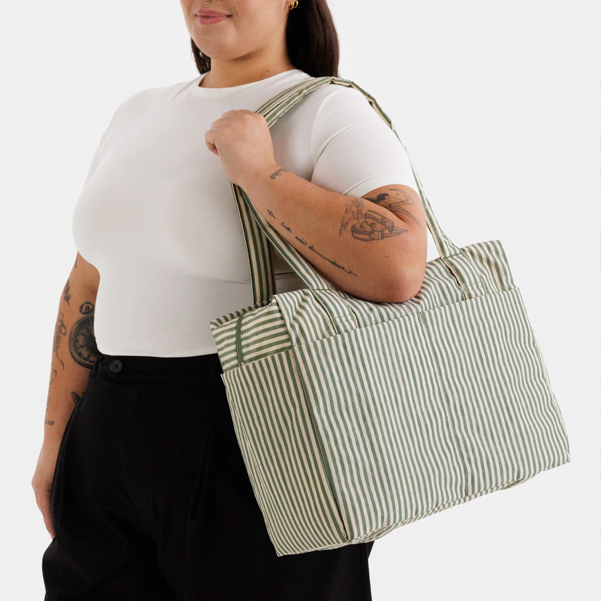 A sage striped nylon carry on bag on a model's shoulder.