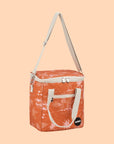 An orange mini cooler bag with a coastal pattern and ivory canvas straps and handles. 