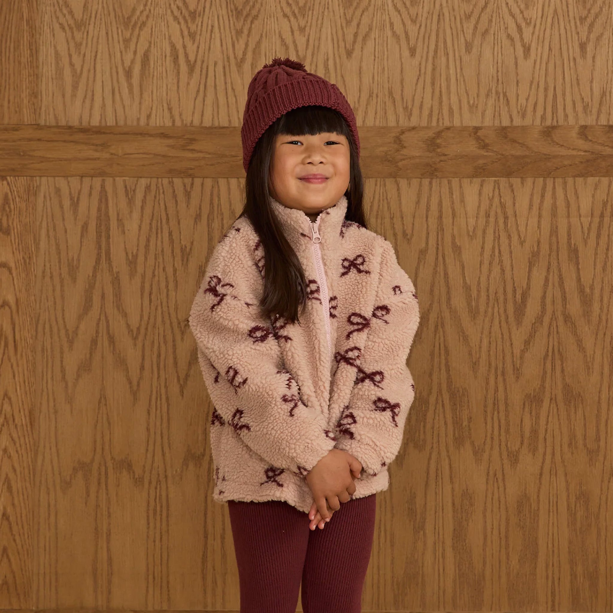 A fuzzy light pink jacket with a dark red bow pattern. 