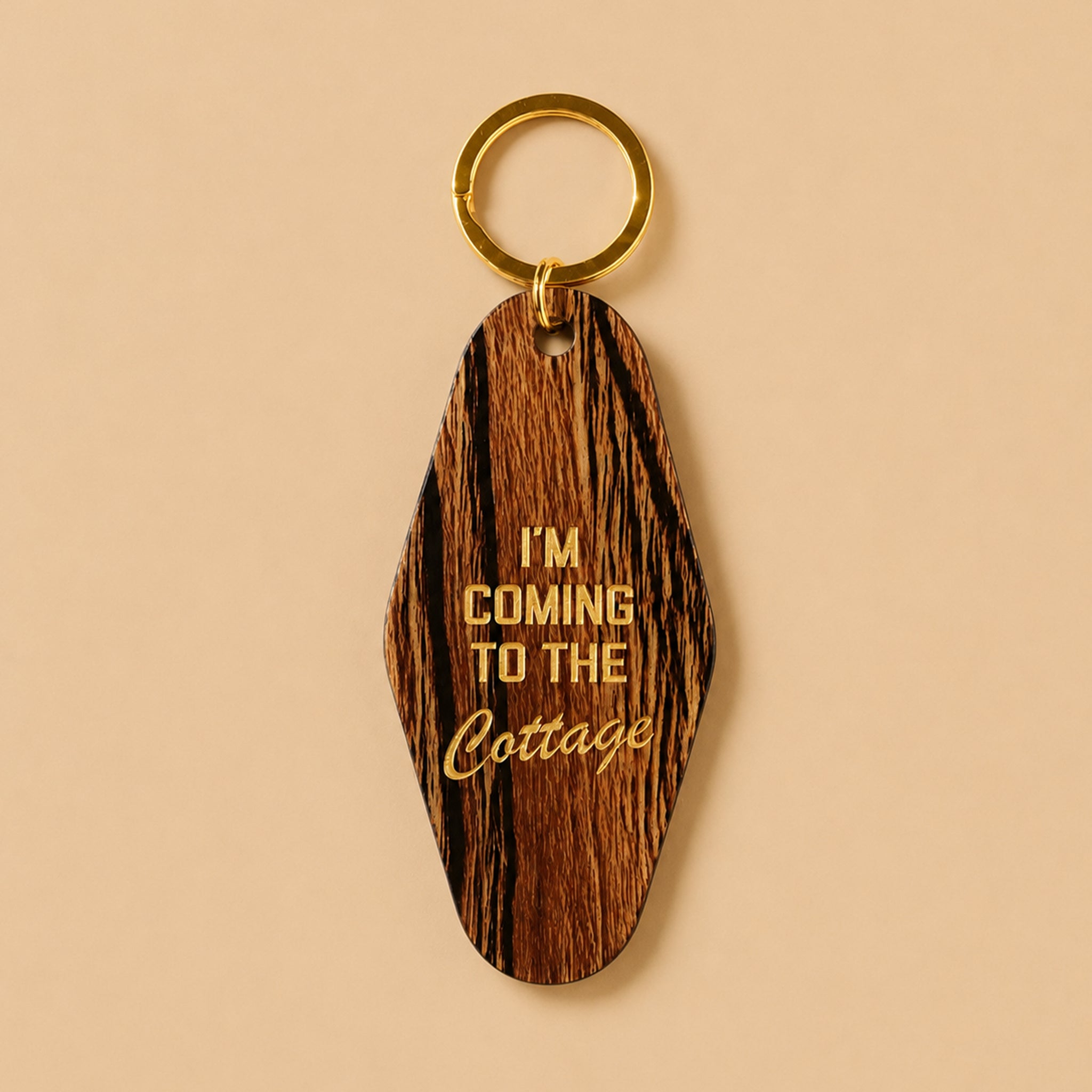 A faux wooden keychain with gold foil text that reads, "I'm Coming To The Cottage". 