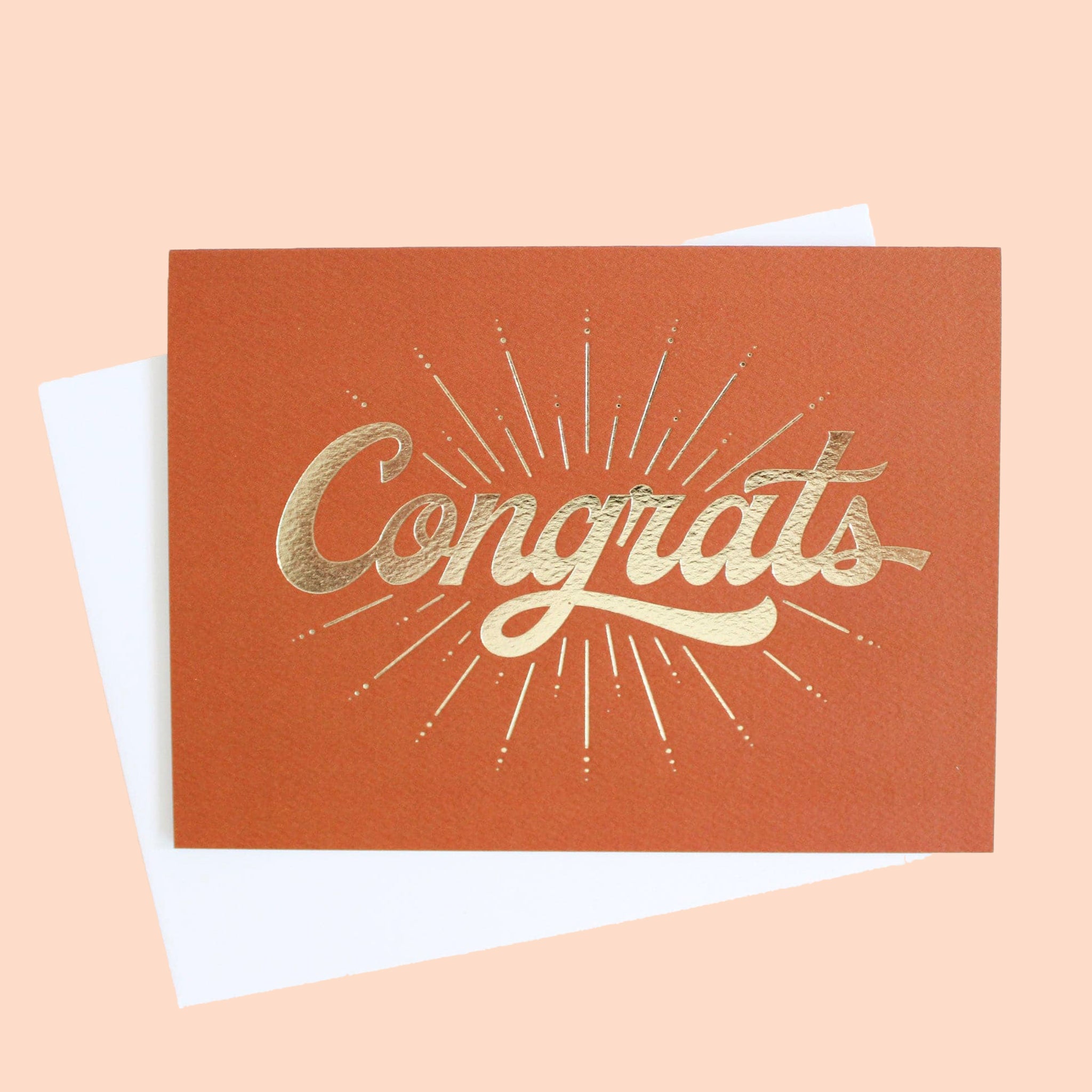 Deep orange colored greeting card with a gold foil starburst design surrounding the word congrats.