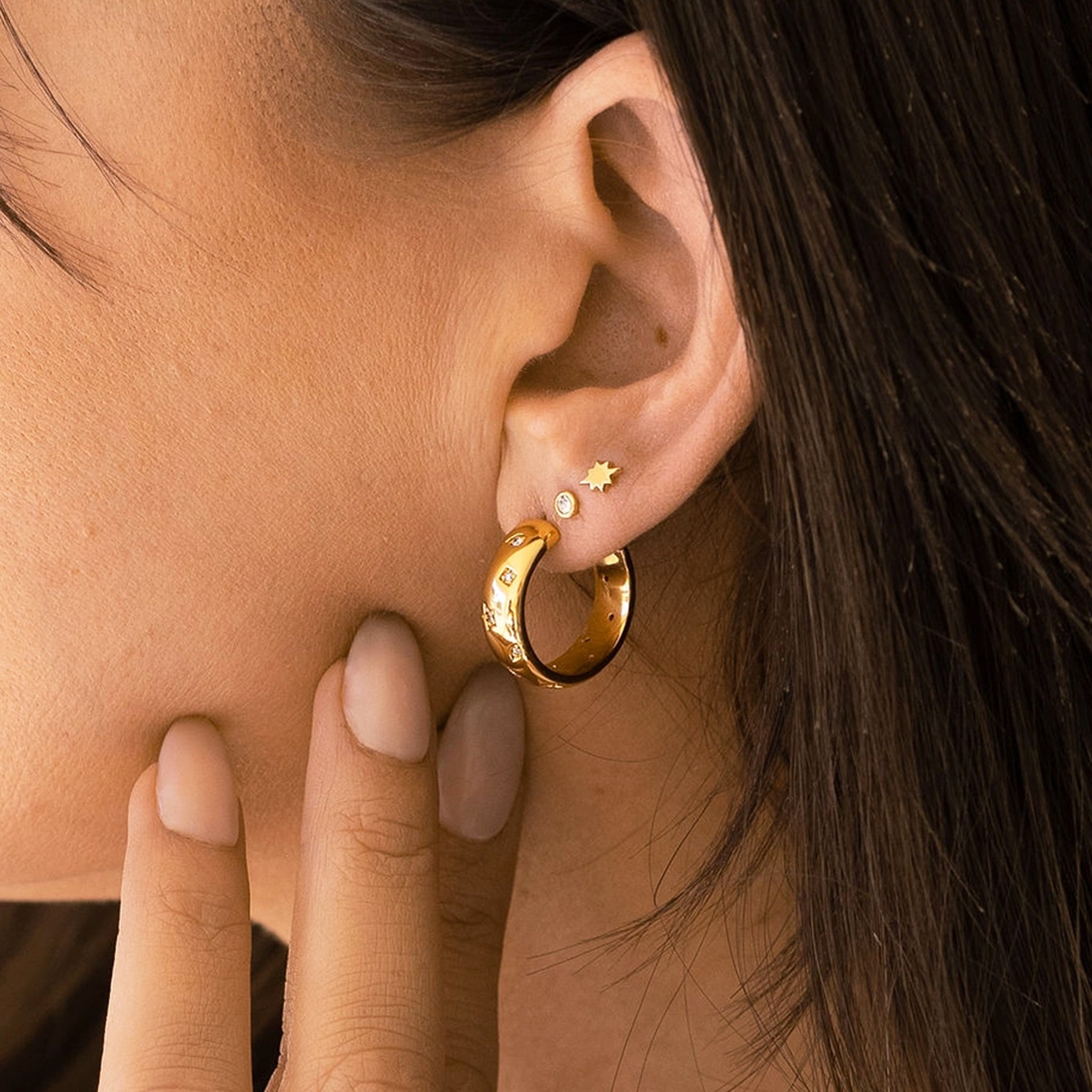 A gold pair of earrings with star, moon and triangle cutouts with cz stones in the center of them. 