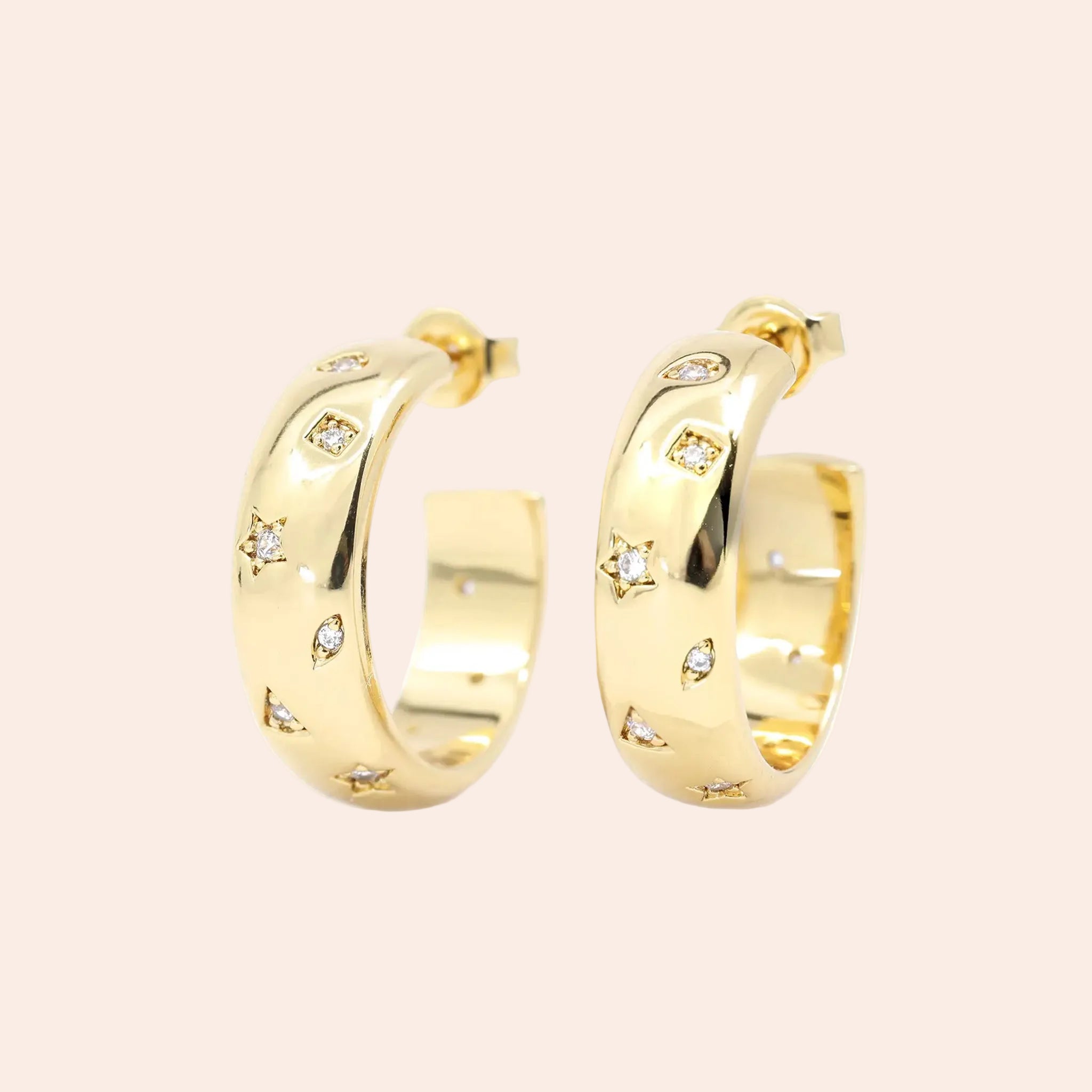 A gold pair of earrings with star, moon and triangle cutouts with cz stones in the center of them. 