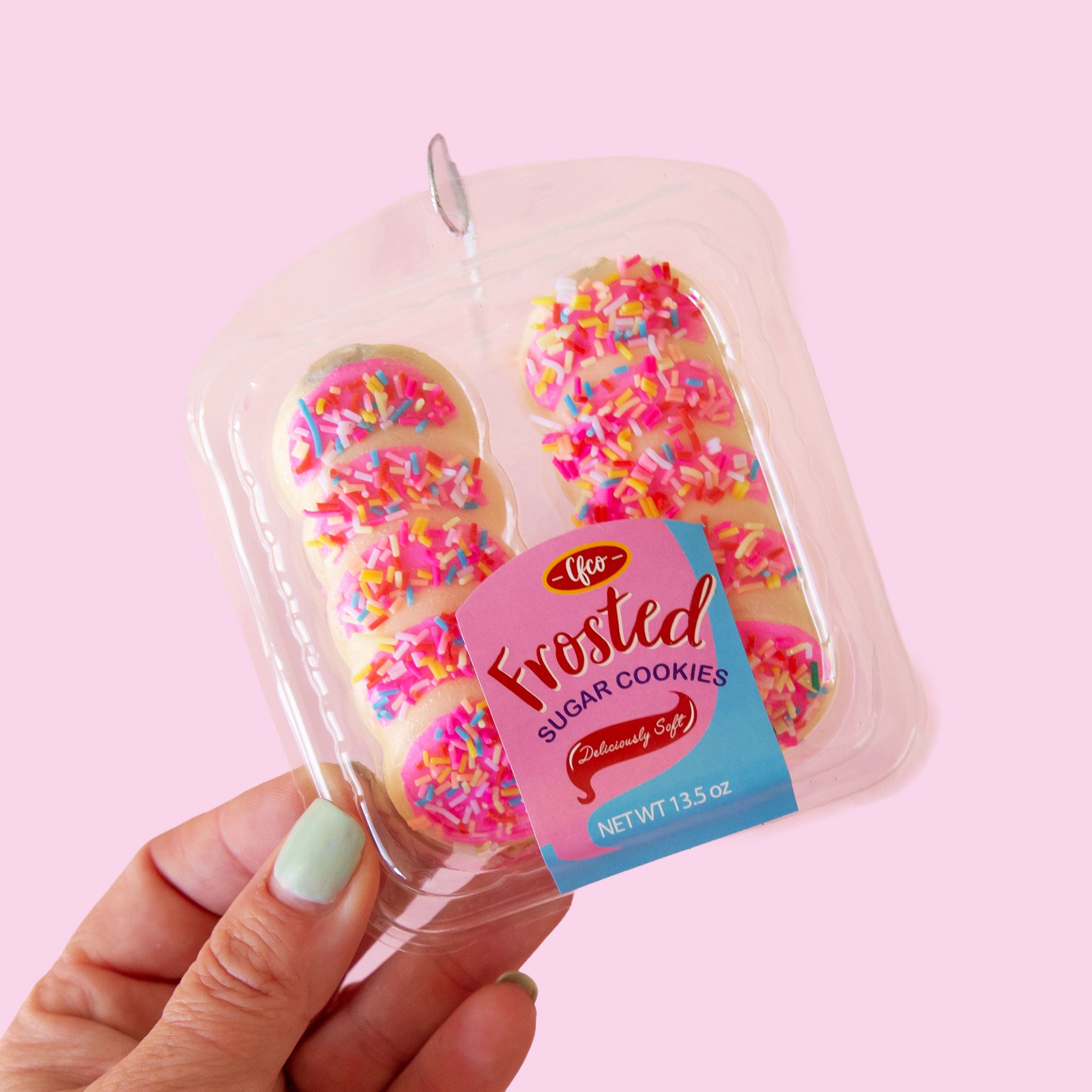 Pack of 10 pink frosted sugar cookies ornament. The cookies are settled in a plastic container and they have colorful sprinkles on the hot pink frosting. 