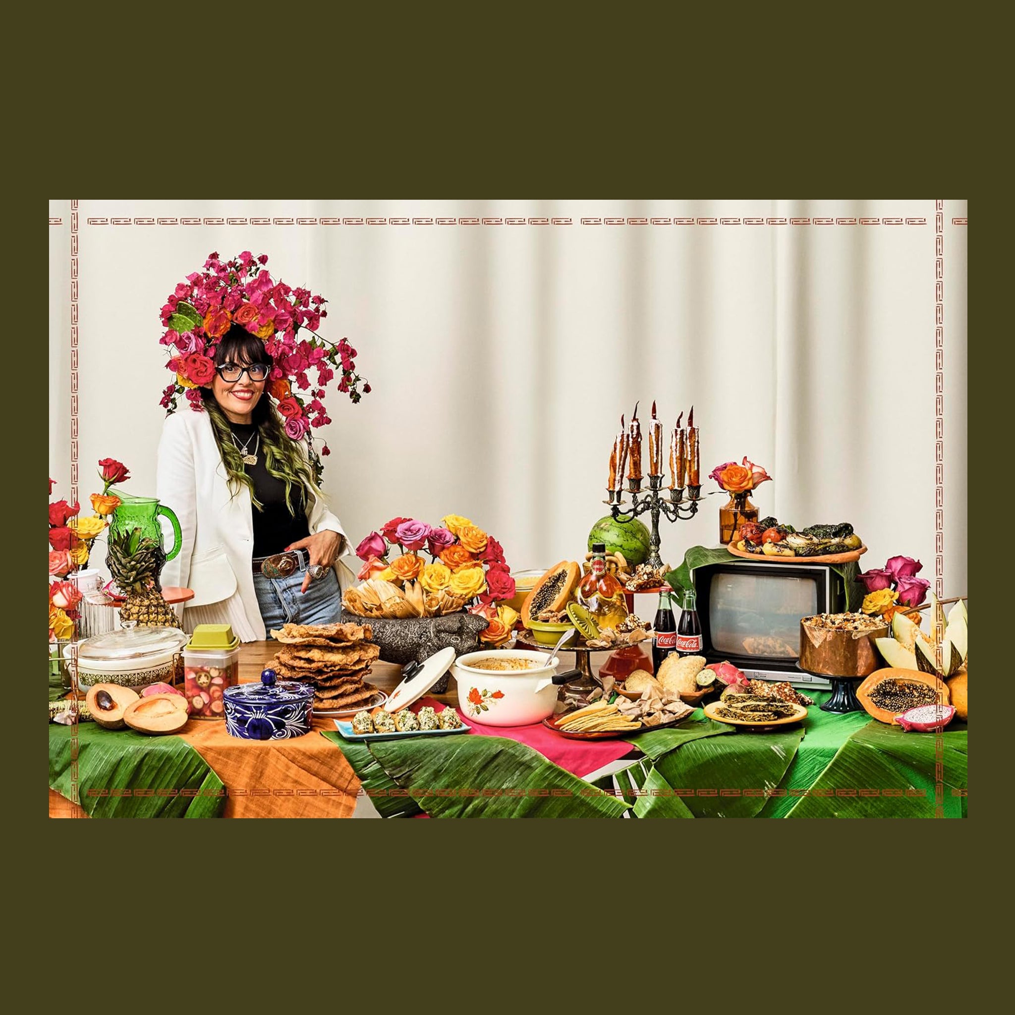 Person with floral headpiece standing behind a table filled with various food items and decorative elements.