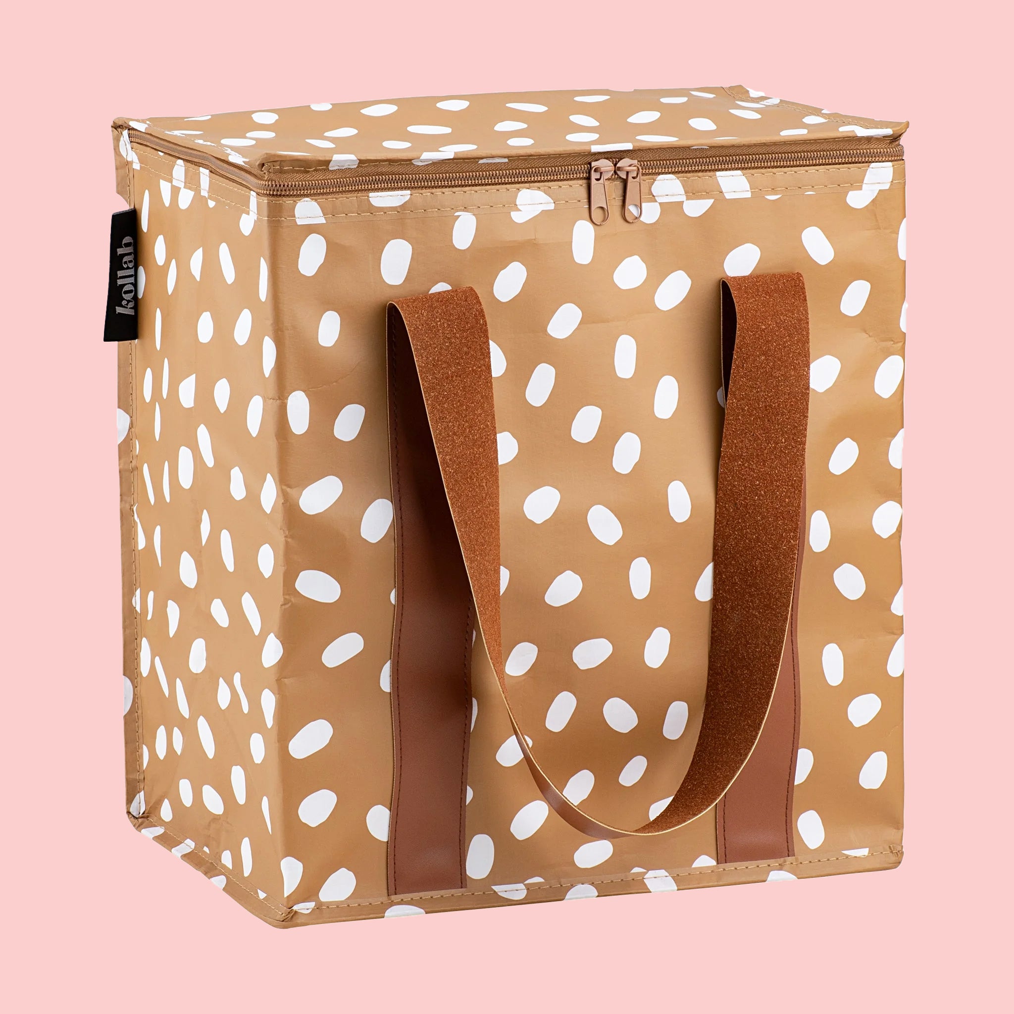 On a pink background is a brown cooler bag with white spots and a darker brown strap. 