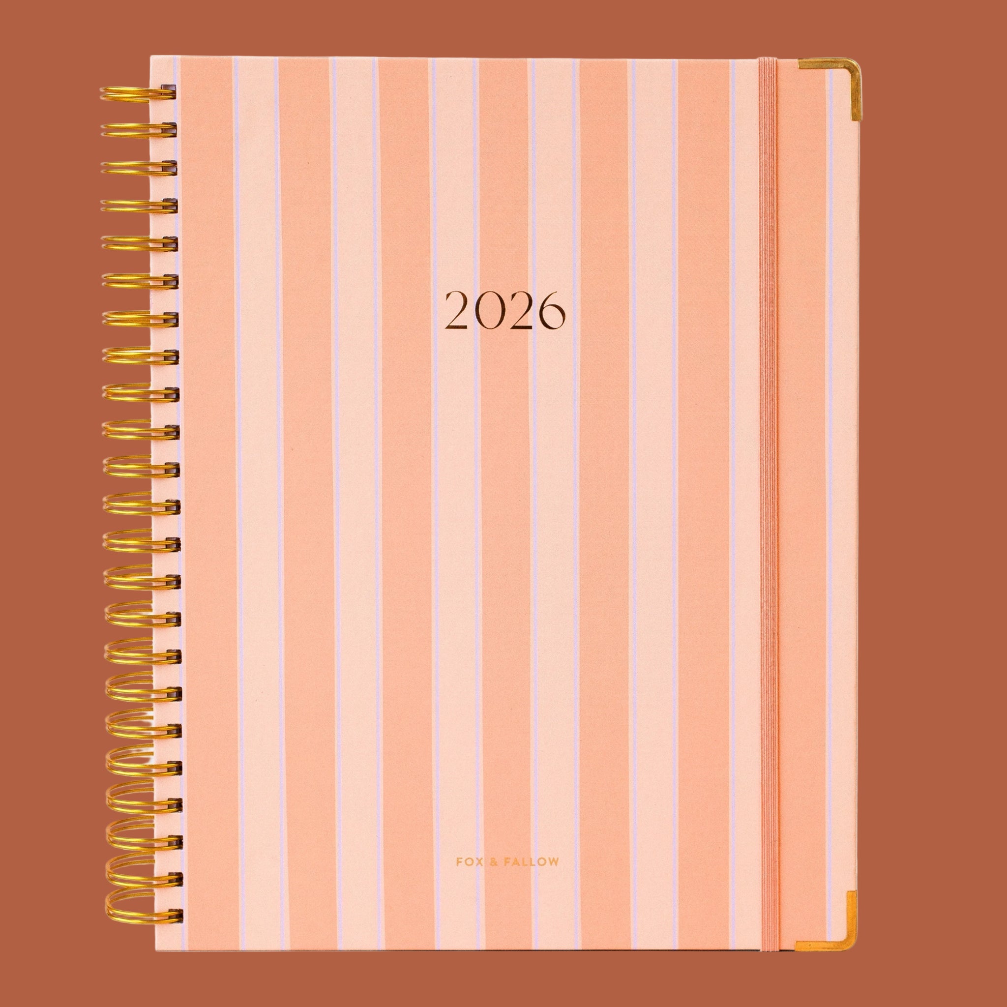 A coral and light blue striped planner with a gold spiral binding and gold foiled text that reads, "2026". 