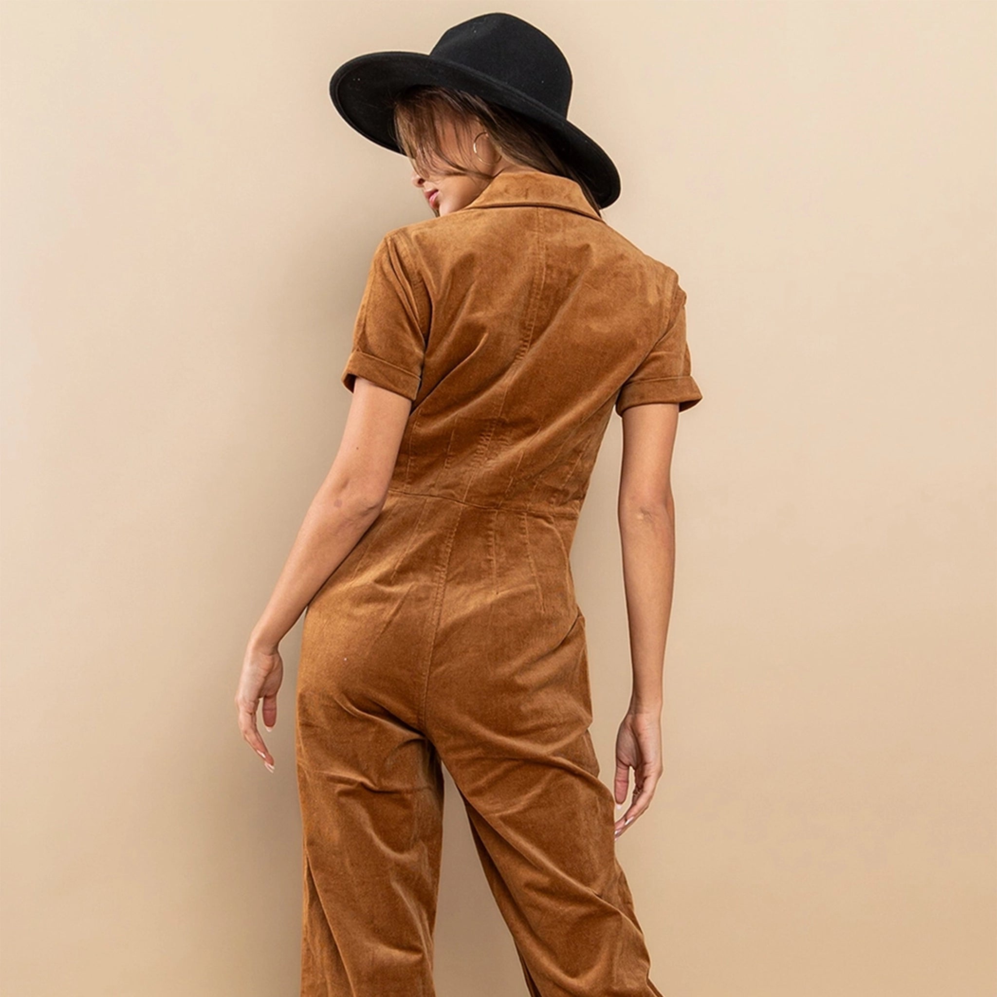 On a tan background is a short sleeved zipper jumpsuit in a camel shade.