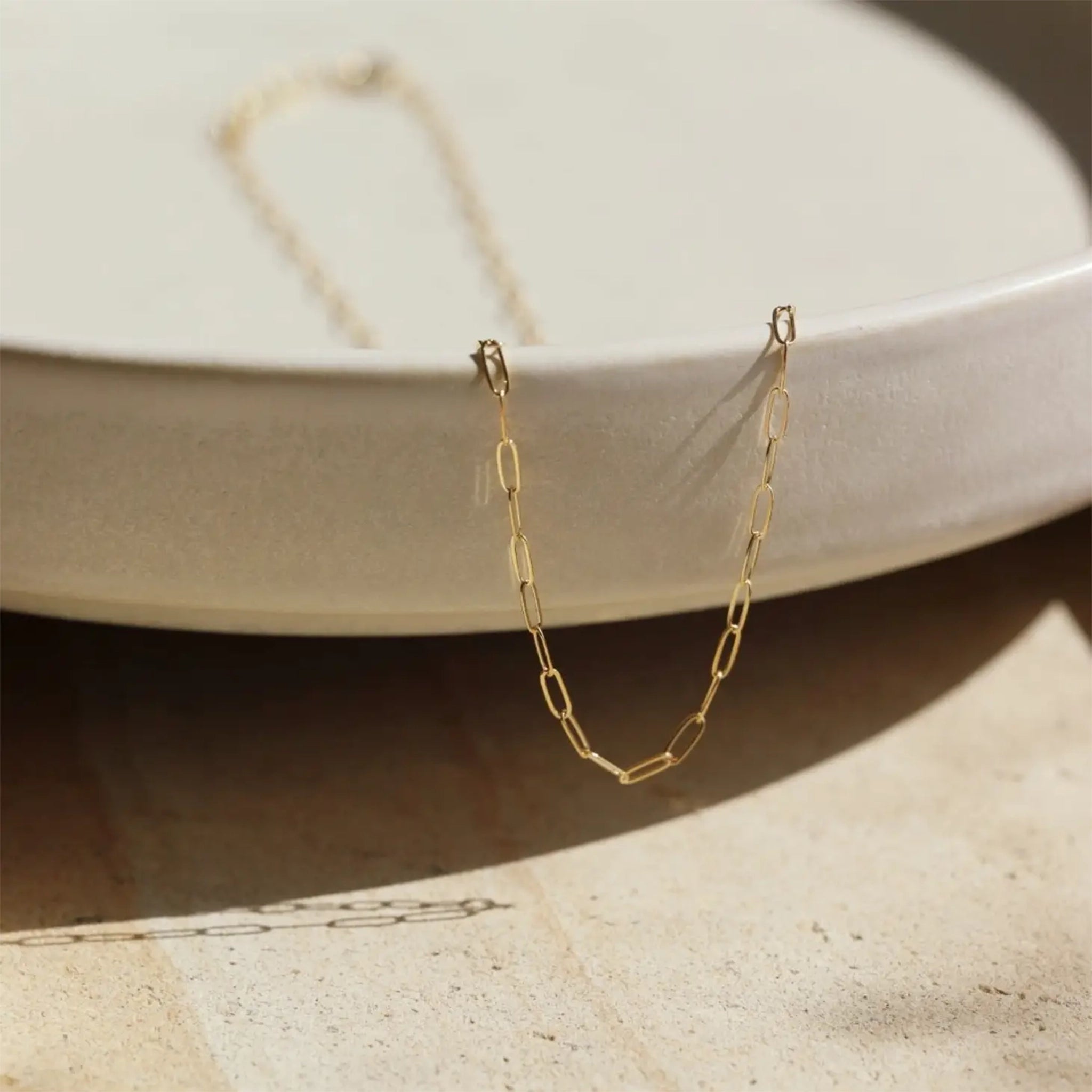 A dainty gold link chain necklace sitting in a ceramic dish. 