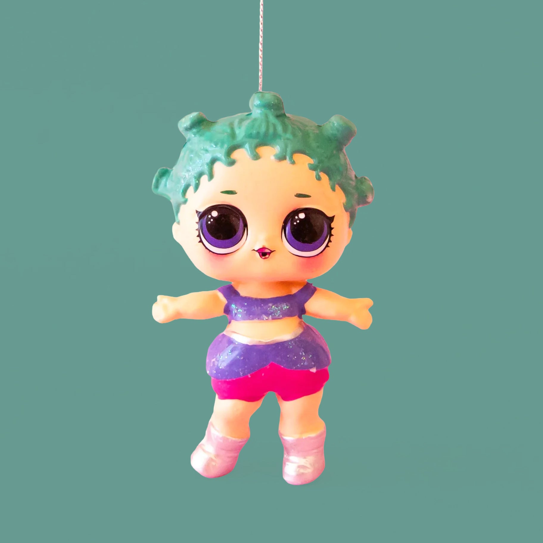 A glass LOL Surprise doll shaped ornament with blueish green hair and a purple outfit. 