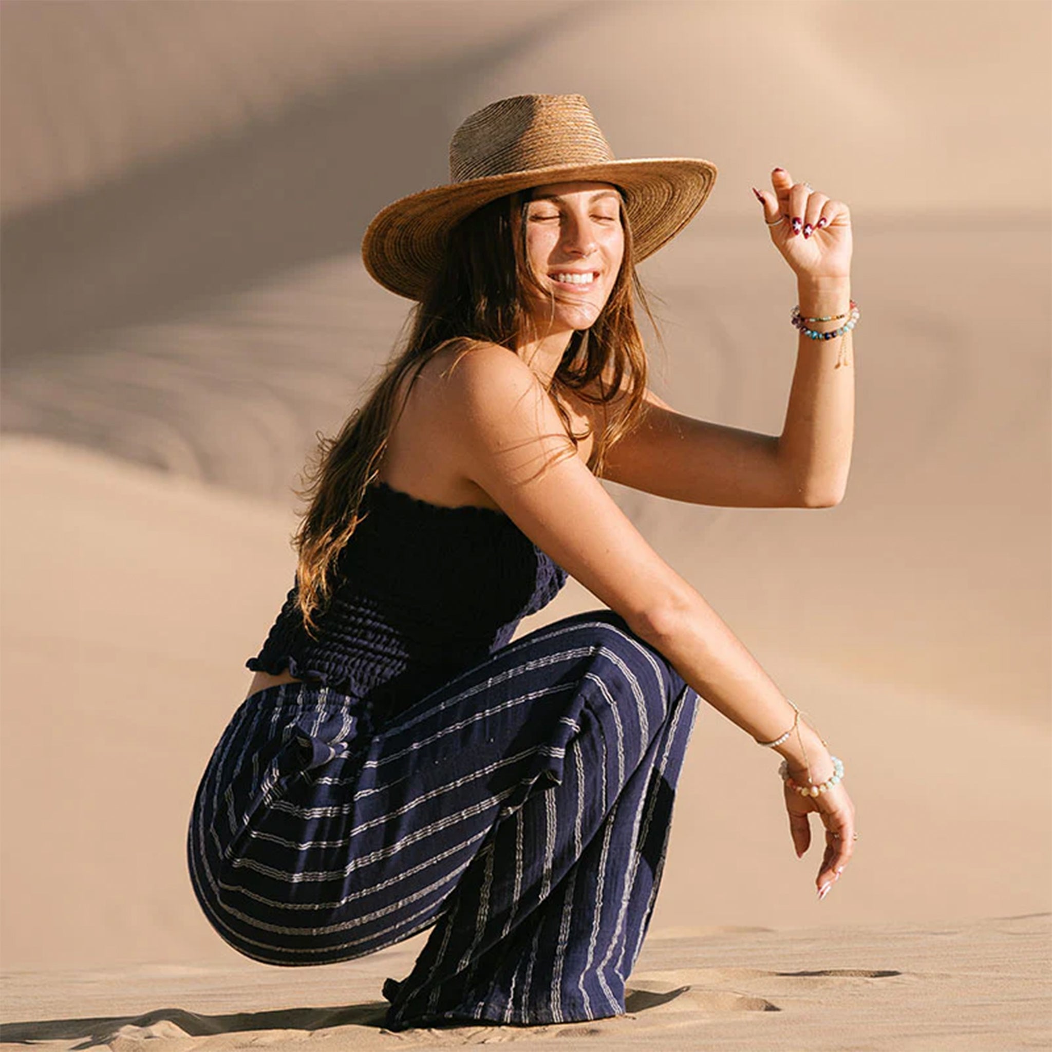 Woman wearing a navy blue top and striped pants on a beige background