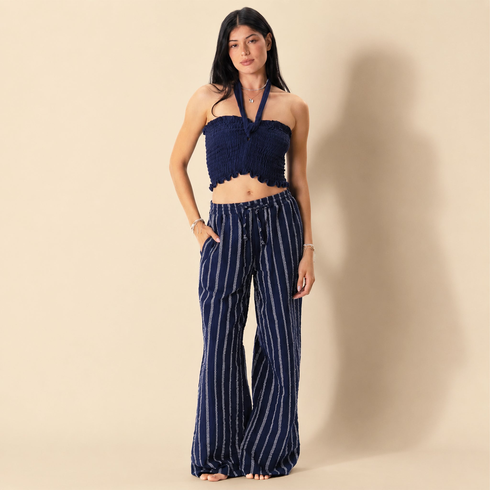Woman wearing a navy blue top and striped pants on a beige background