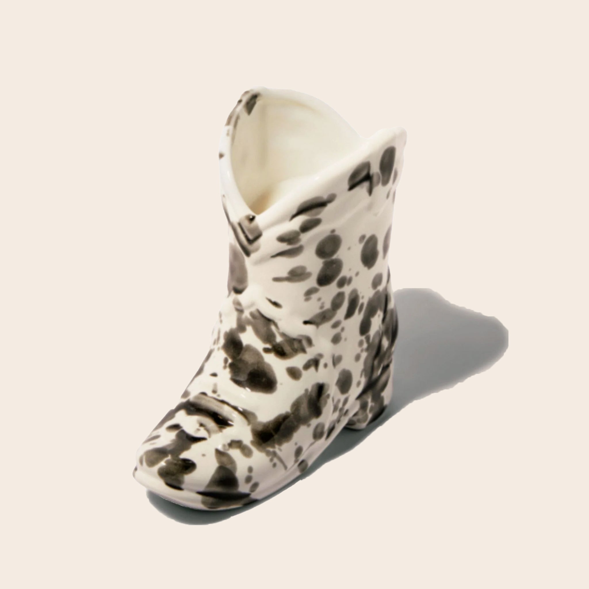 A black and white speckled ceramic boot shaped candle. 