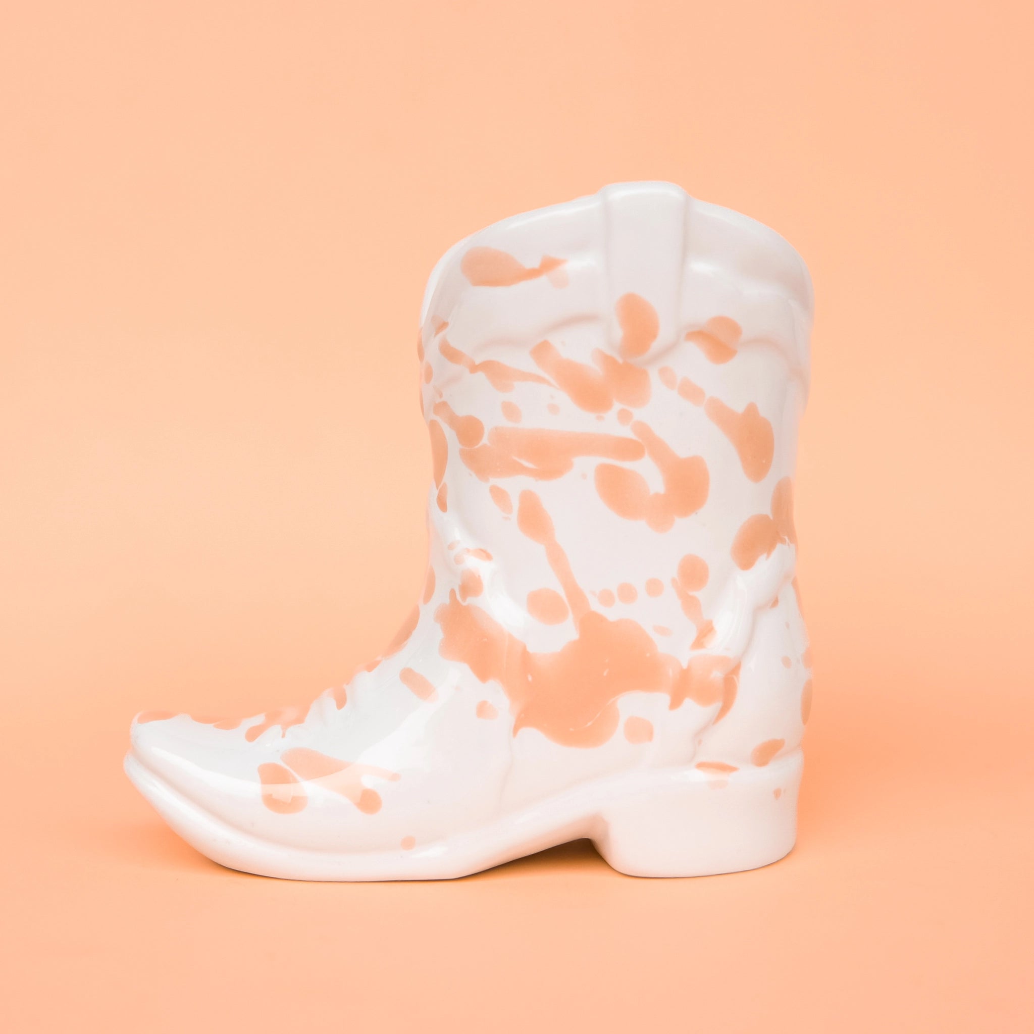 On a peachy background is a white and peach speckled cowboy boot shaped candle. 