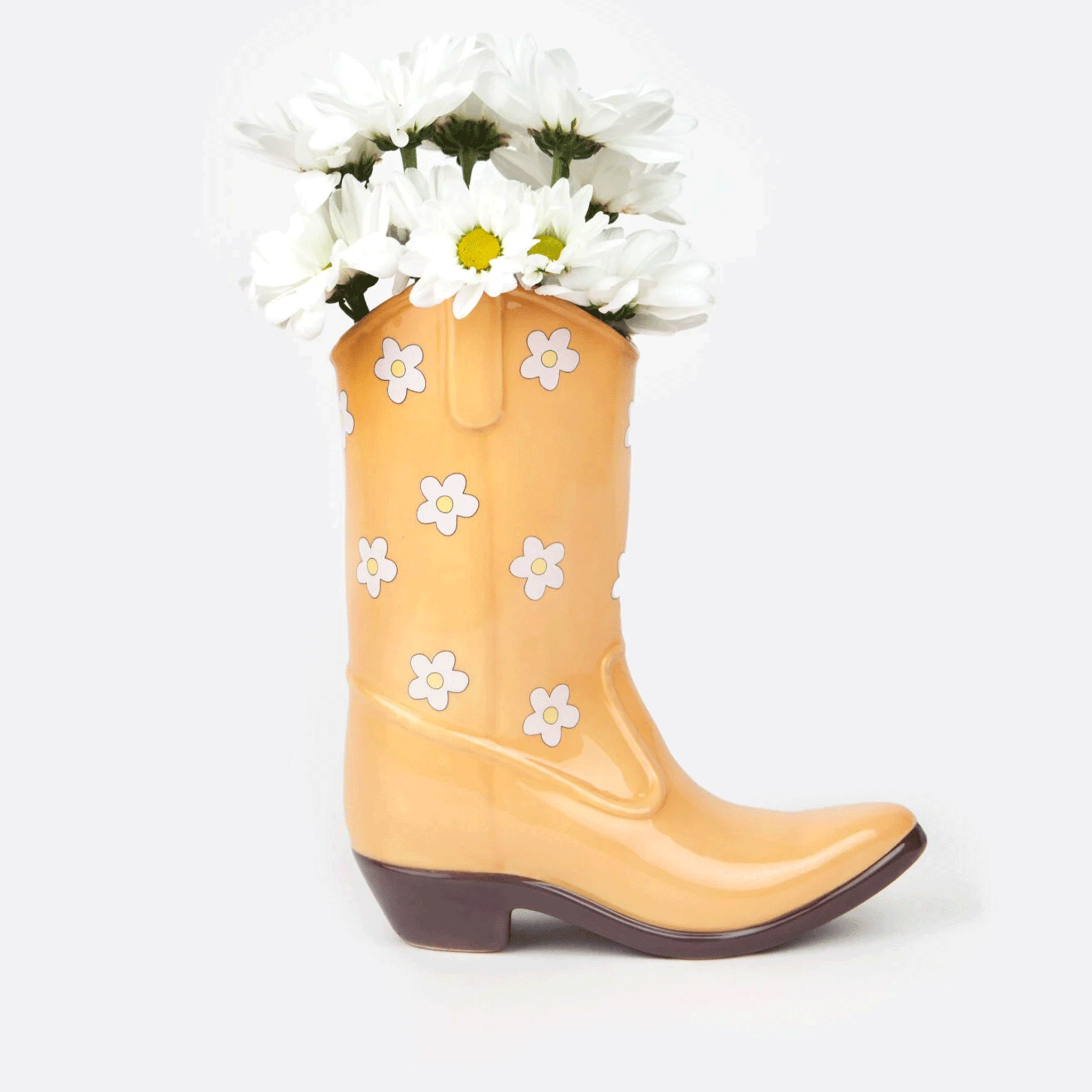 On a white background is a yellow cowboy boot shaped vase with white and yellow daisy print all over. Flowers not included with purchase. 