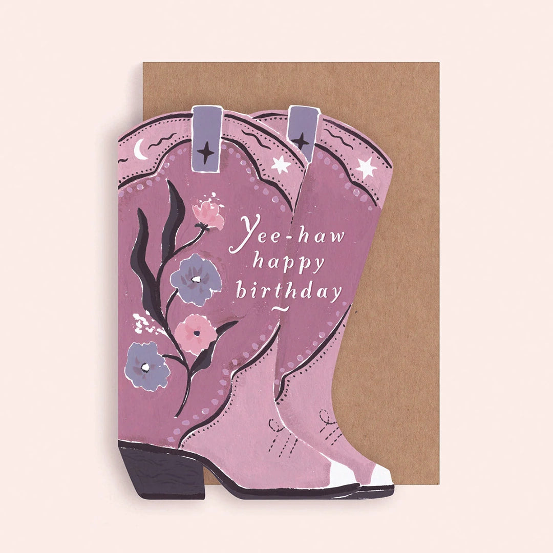 A purple card in the shape of cowgirl boots with a floral design on it as well as white text that reads, &quot;Yee-haw happy birthday&quot;.