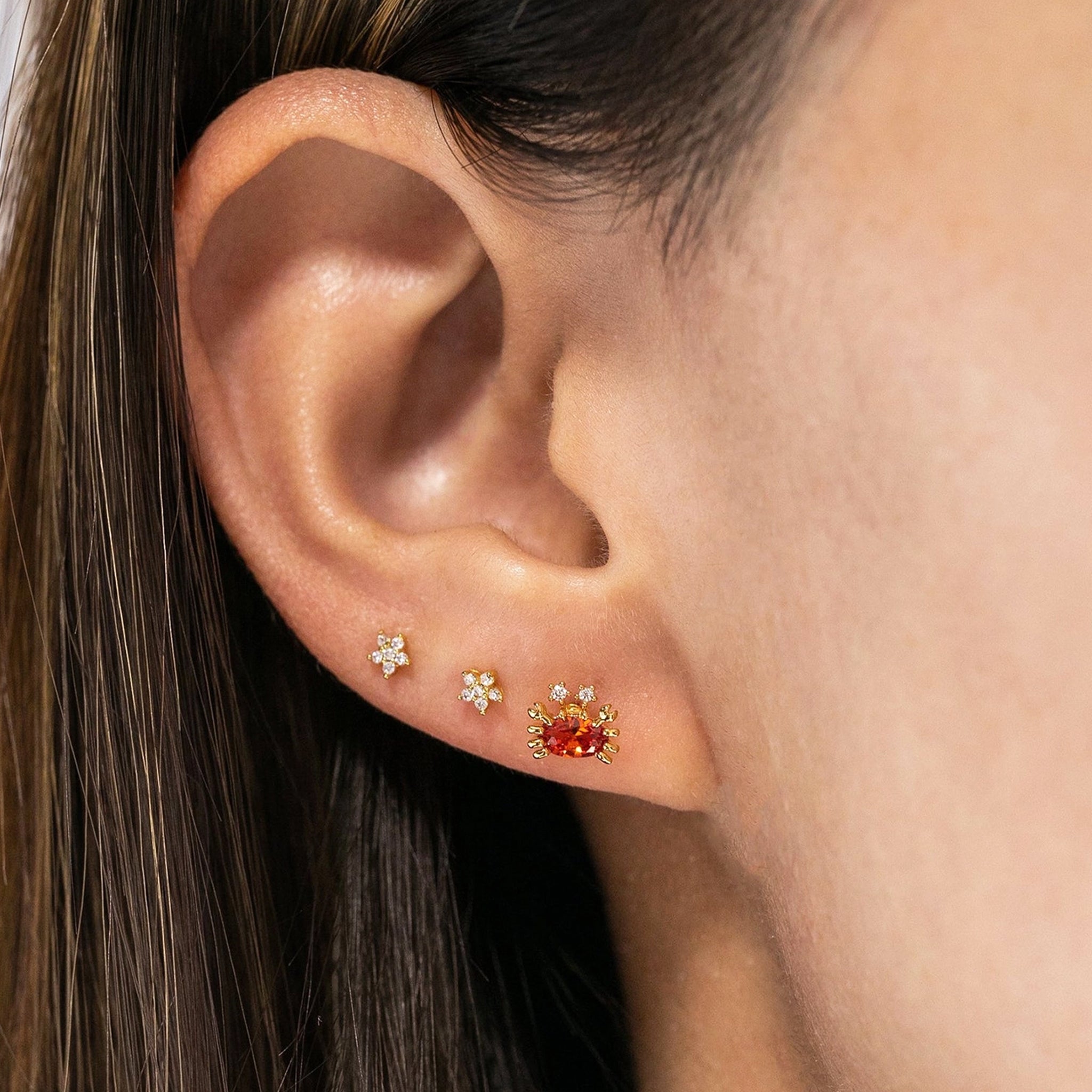 A pair of crab shaped stud earrings with cz stones and a reddish orange stone in the center. 
